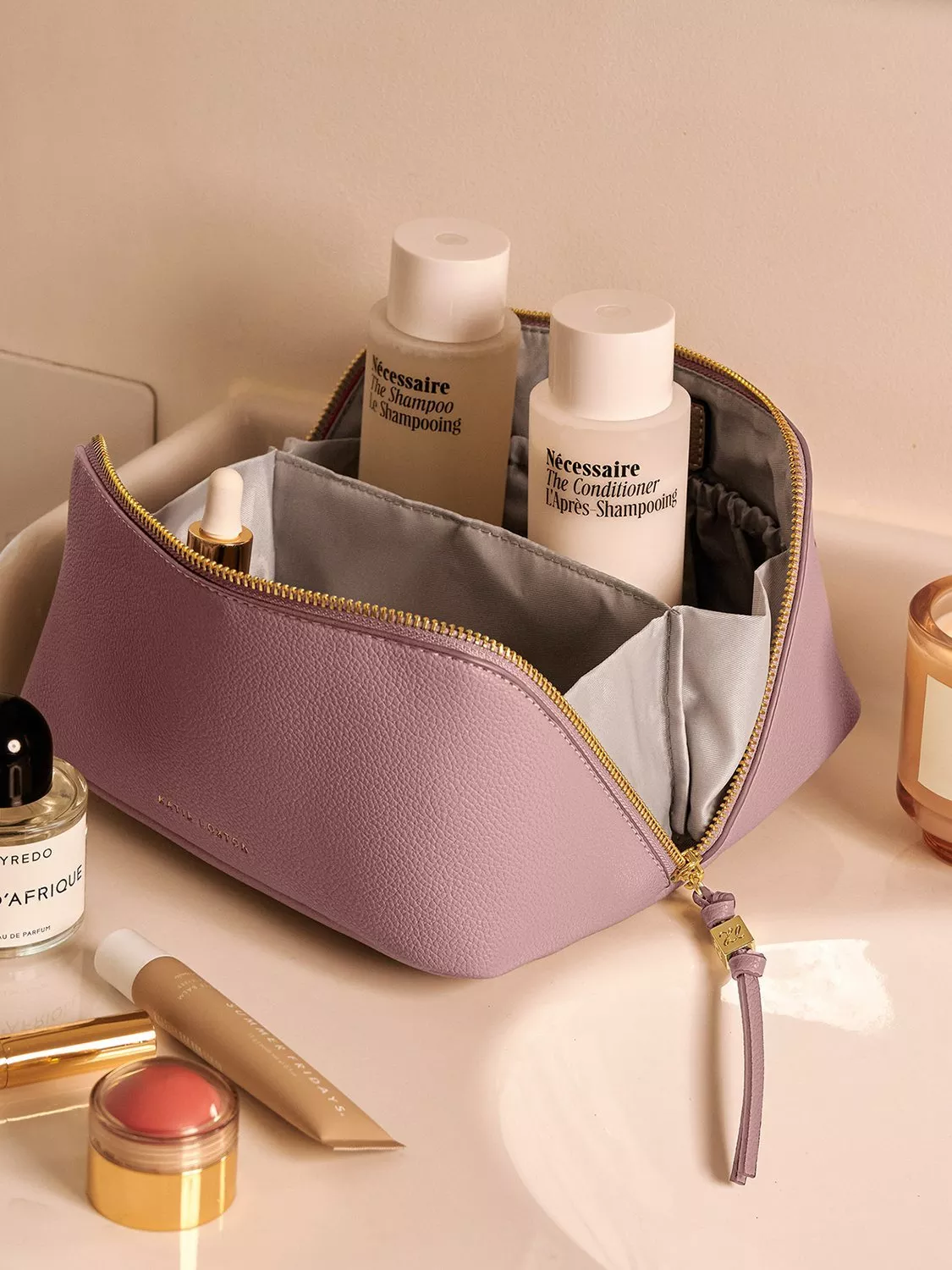 Lavender leather wash bag with shampoo and conditioner bottles, cosmetics and perfume on bathroom counter.