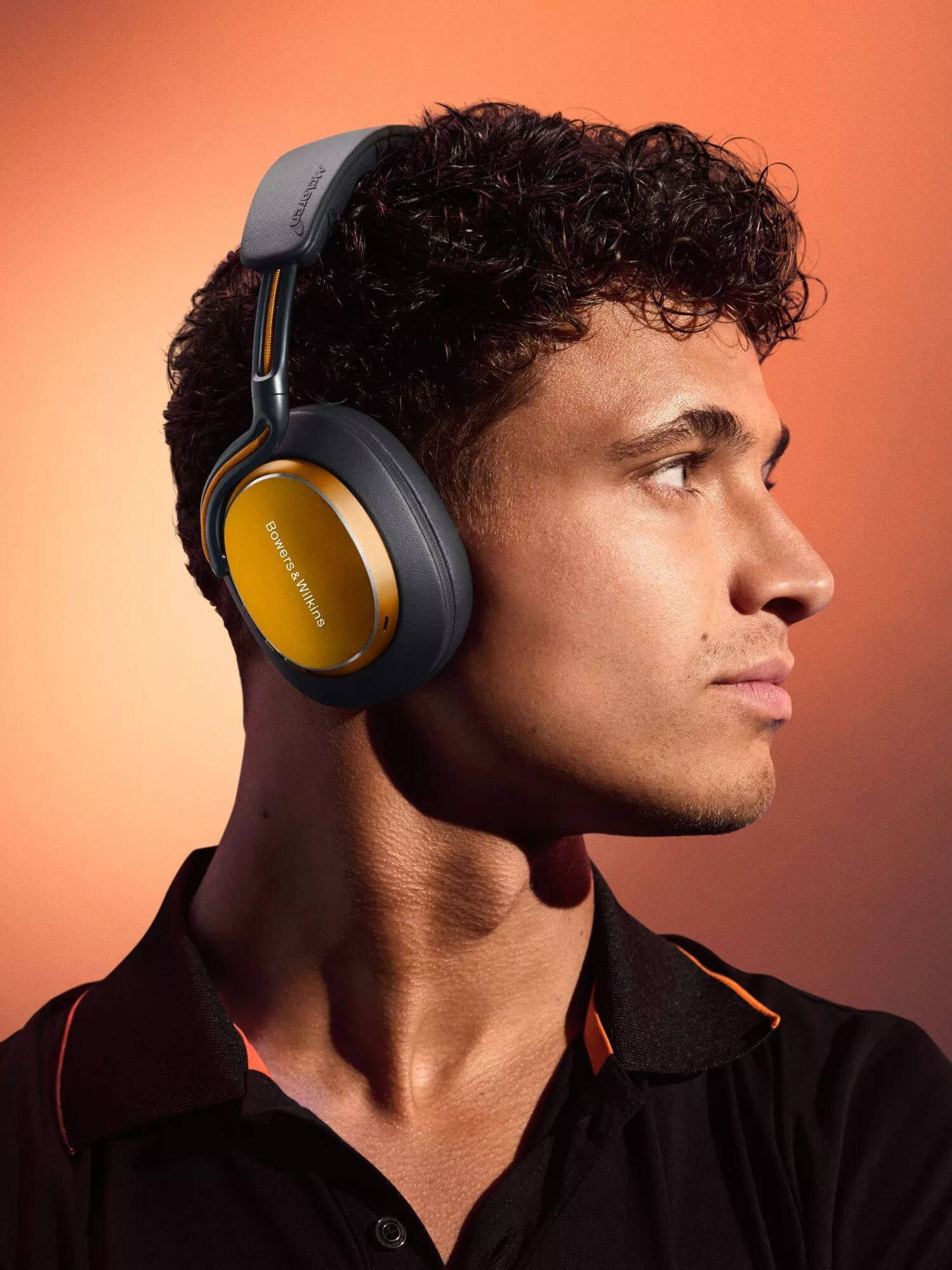 Side profile of man wearing Bowers & Wilkins wireless over-ear headphones, studio portrait on warm background