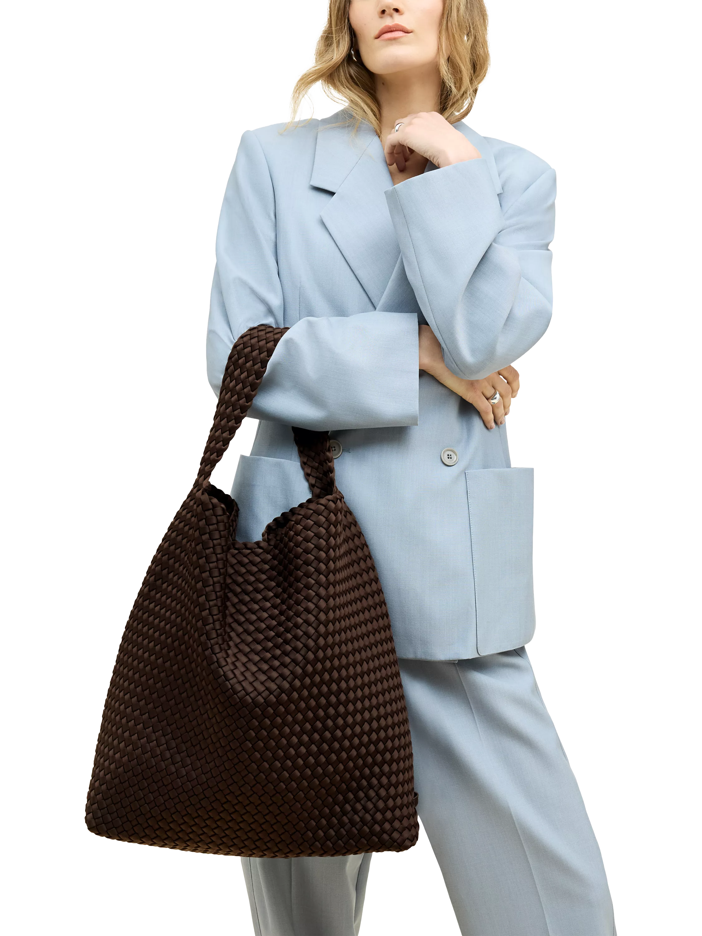 A person in a stylish blue suit holding a large, textured brown woven handbag, posing confidently.