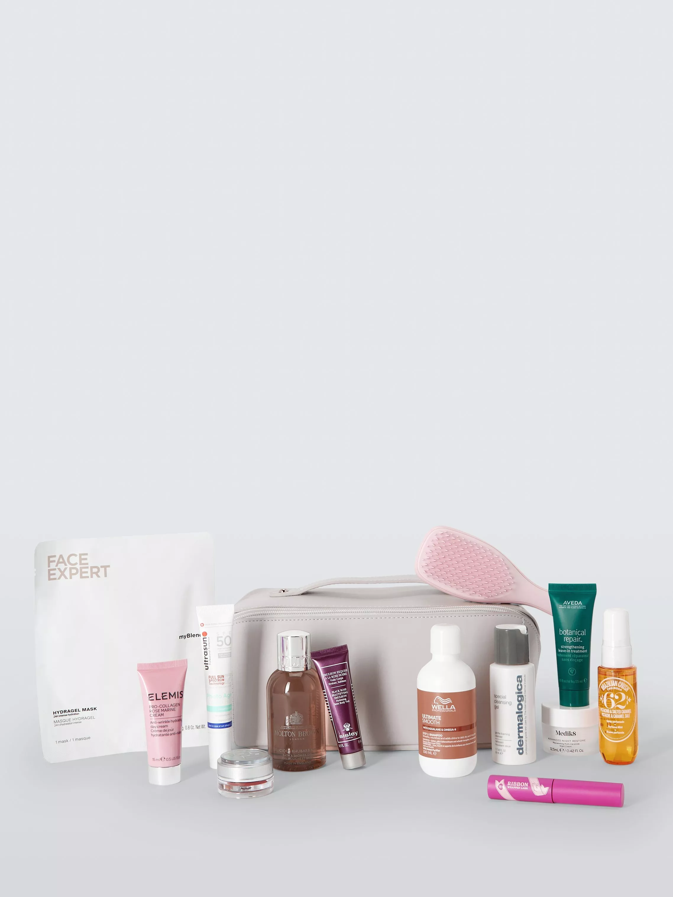 Beauty travel kit with skincare, shampoo, cleanser, SPF and hair brush arranged in front of a grey wash bag
