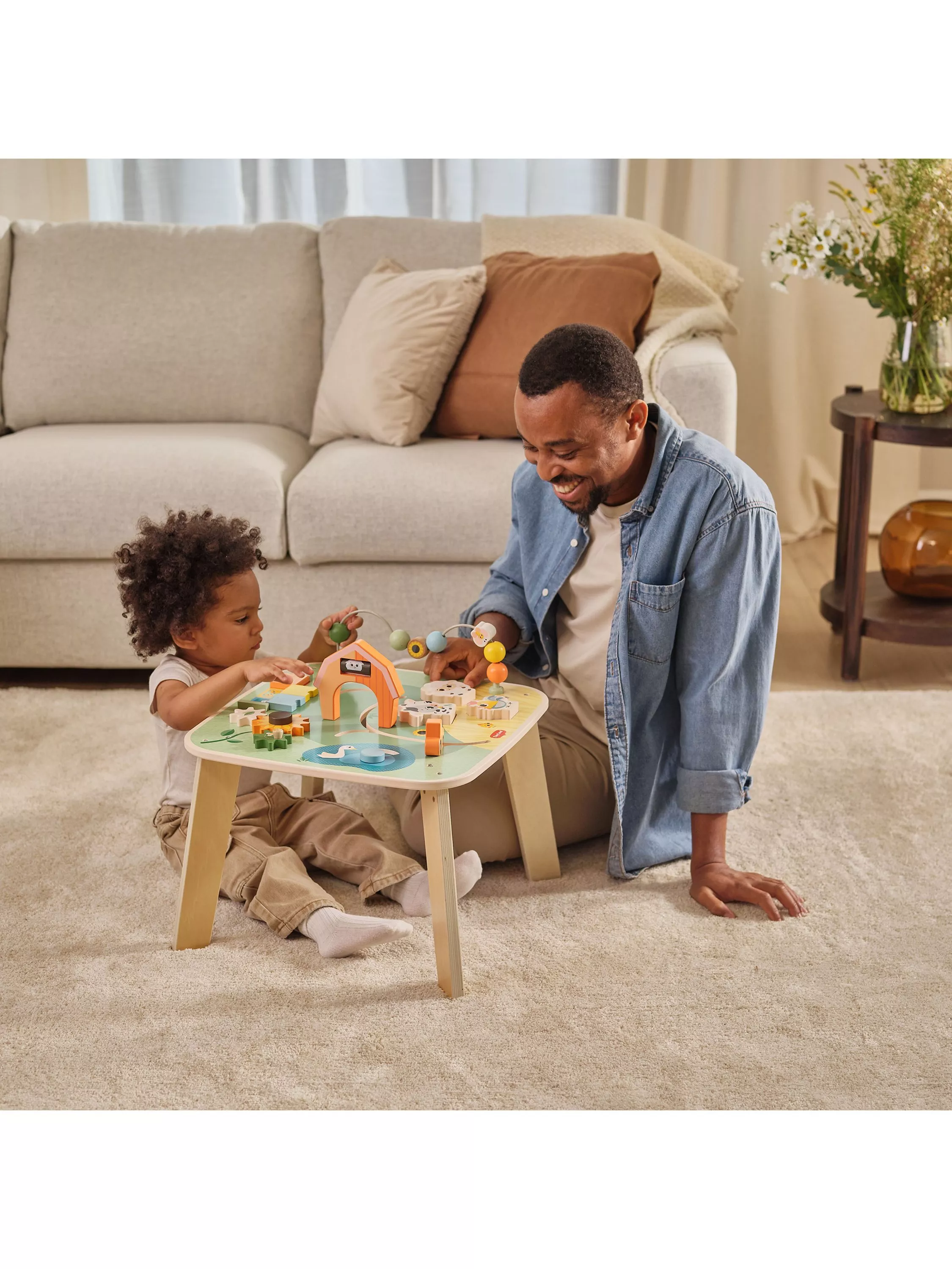 Father and toddler playing with a colourful wooden activity table toy in a cosy living room at home