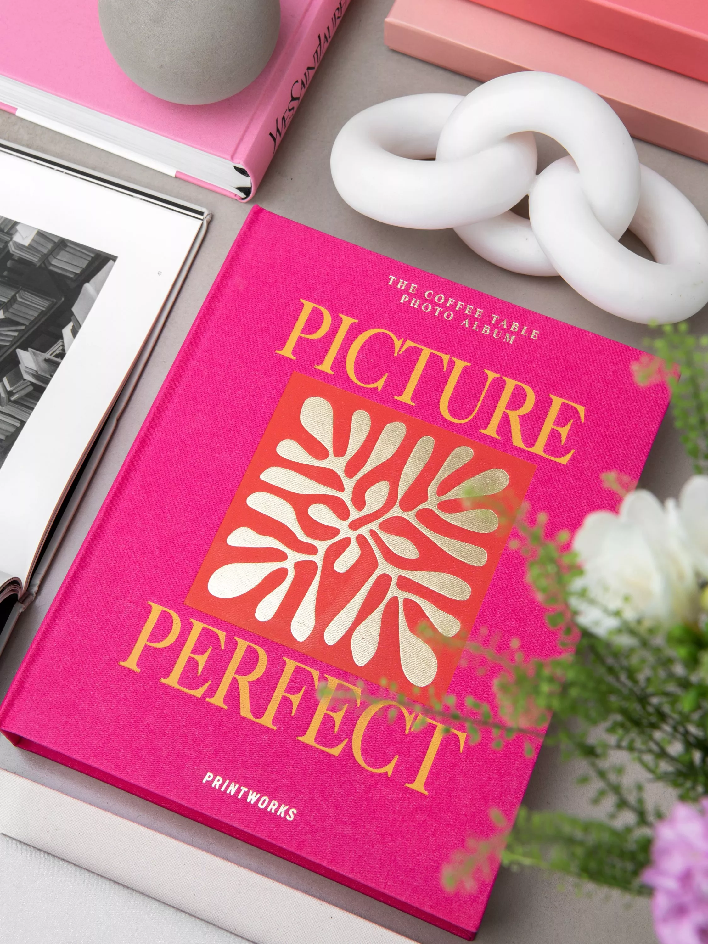Pink coffee table book on a modern tabletop with white chain sculpture, art book and soft floral styling