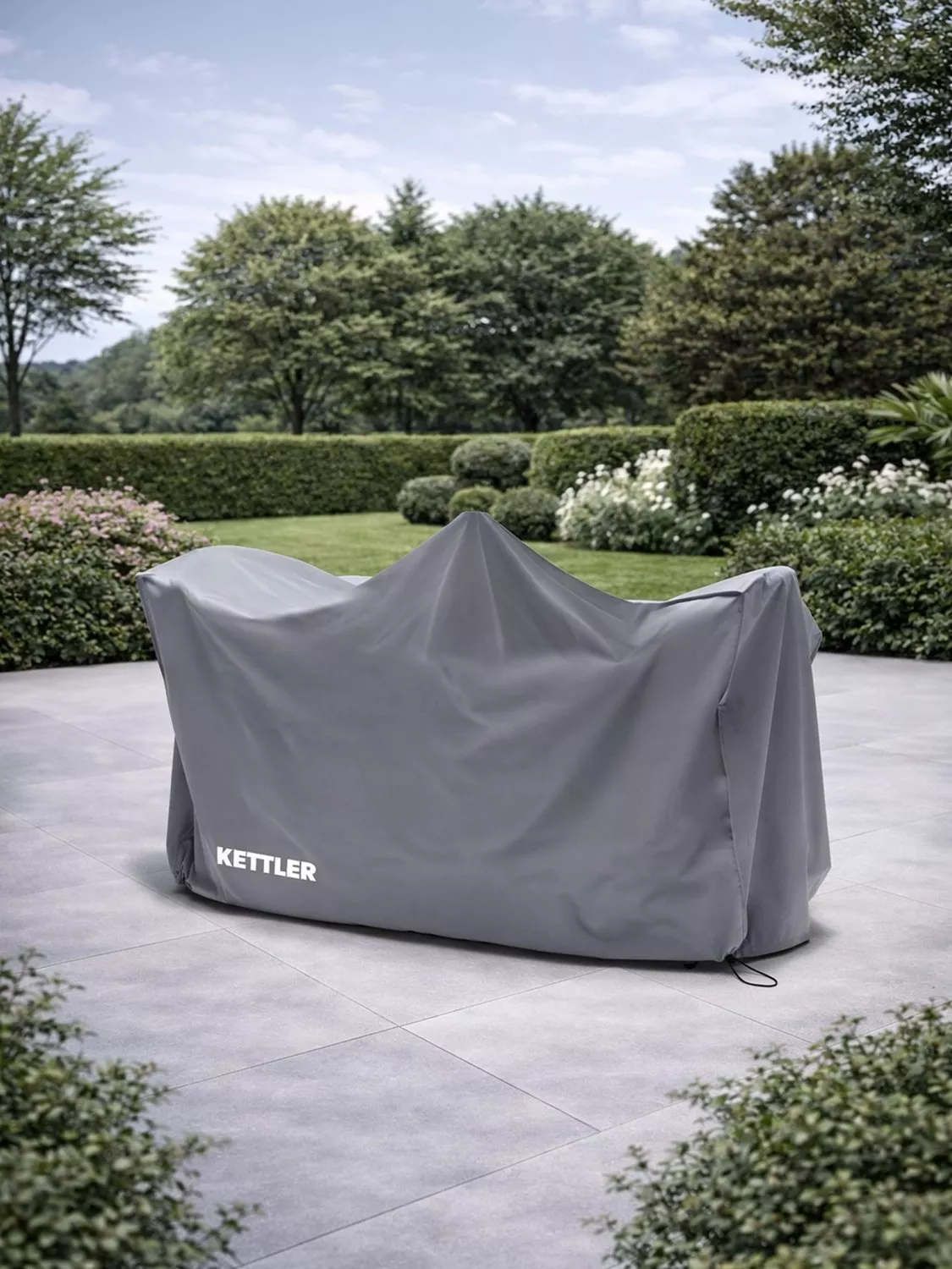 Kettler waterproof outdoor furniture cover on patio, protecting garden seating from rain and sun in landscaped garden