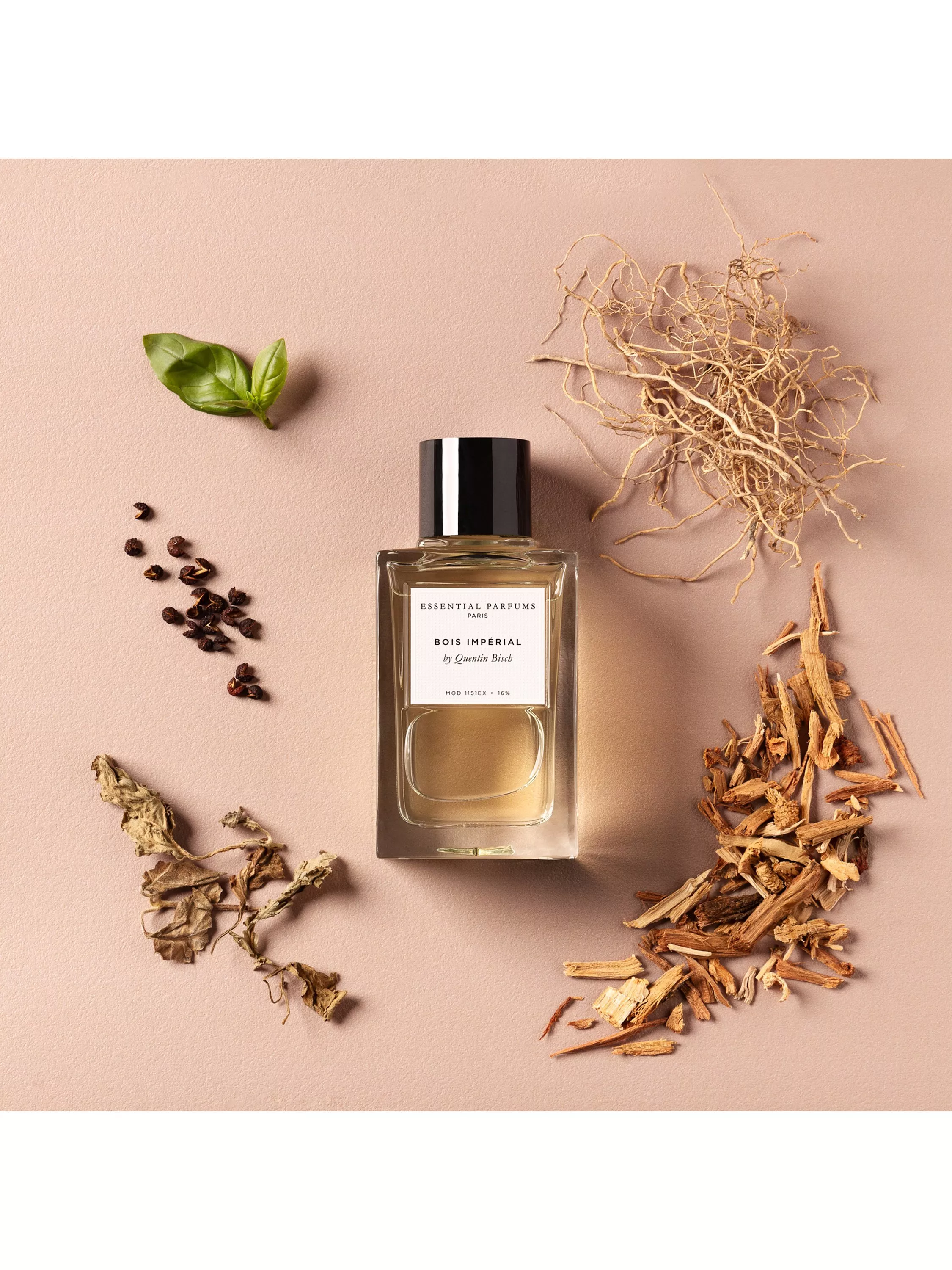 Essential Parfums Bois Impérial perfume bottle on beige backdrop with basil leaf, peppercorns and woody notes.