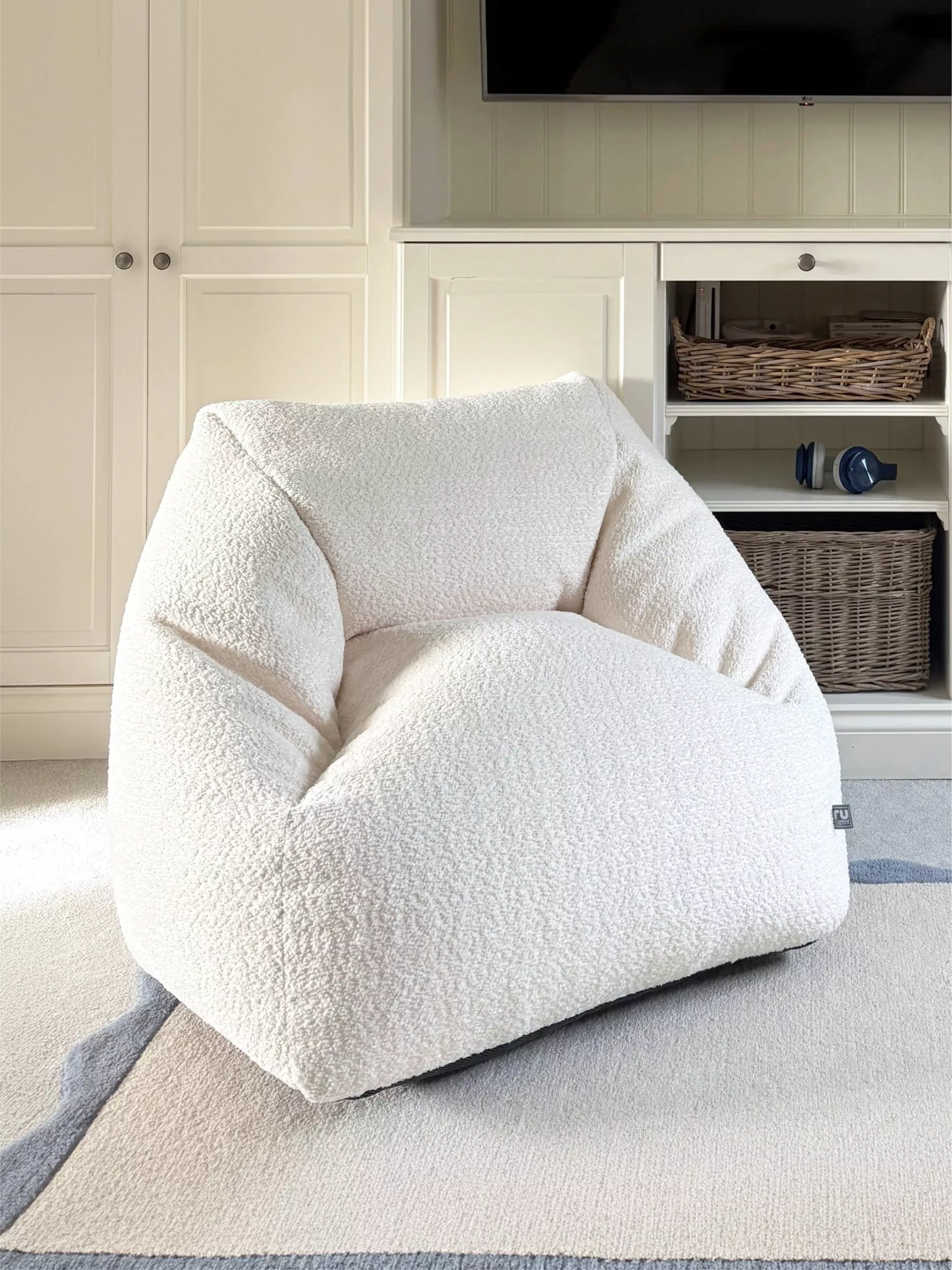 Cream teddy boucle accent chair in modern living room with built-in shelves, TV unit and woven baskets storage
