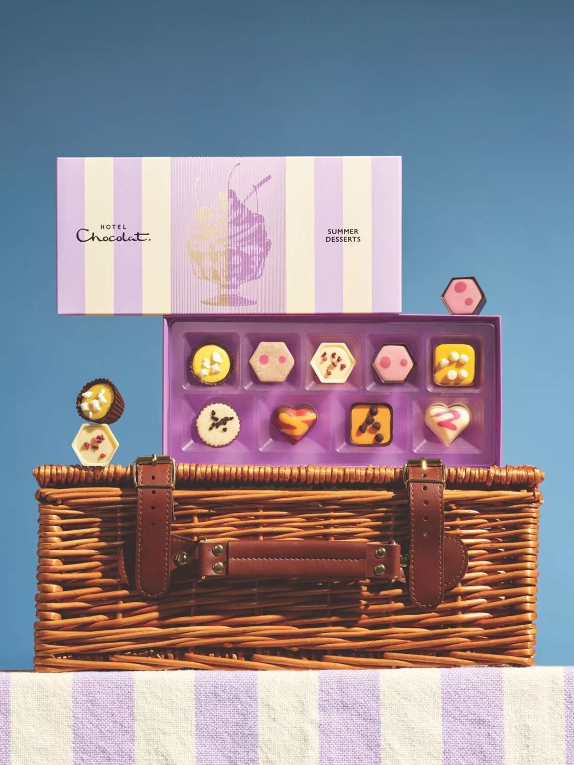 Open Hotel Chocolat Summer Desserts chocolate box on wicker picnic basket with assorted pralines on blue backdrop