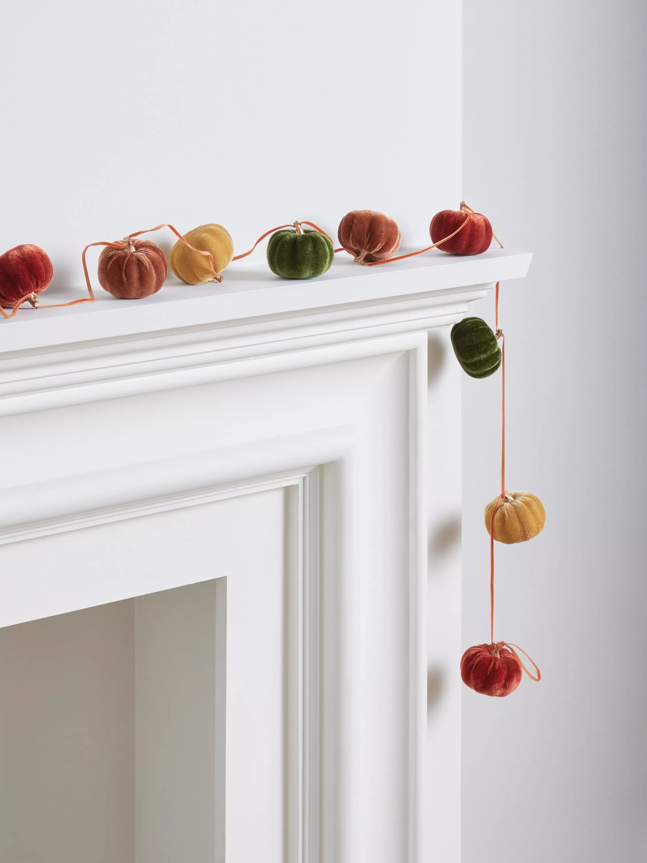 Velvet pumpkin garland in autumn colours draped over a white mantelpiece, cosy seasonal home décor display