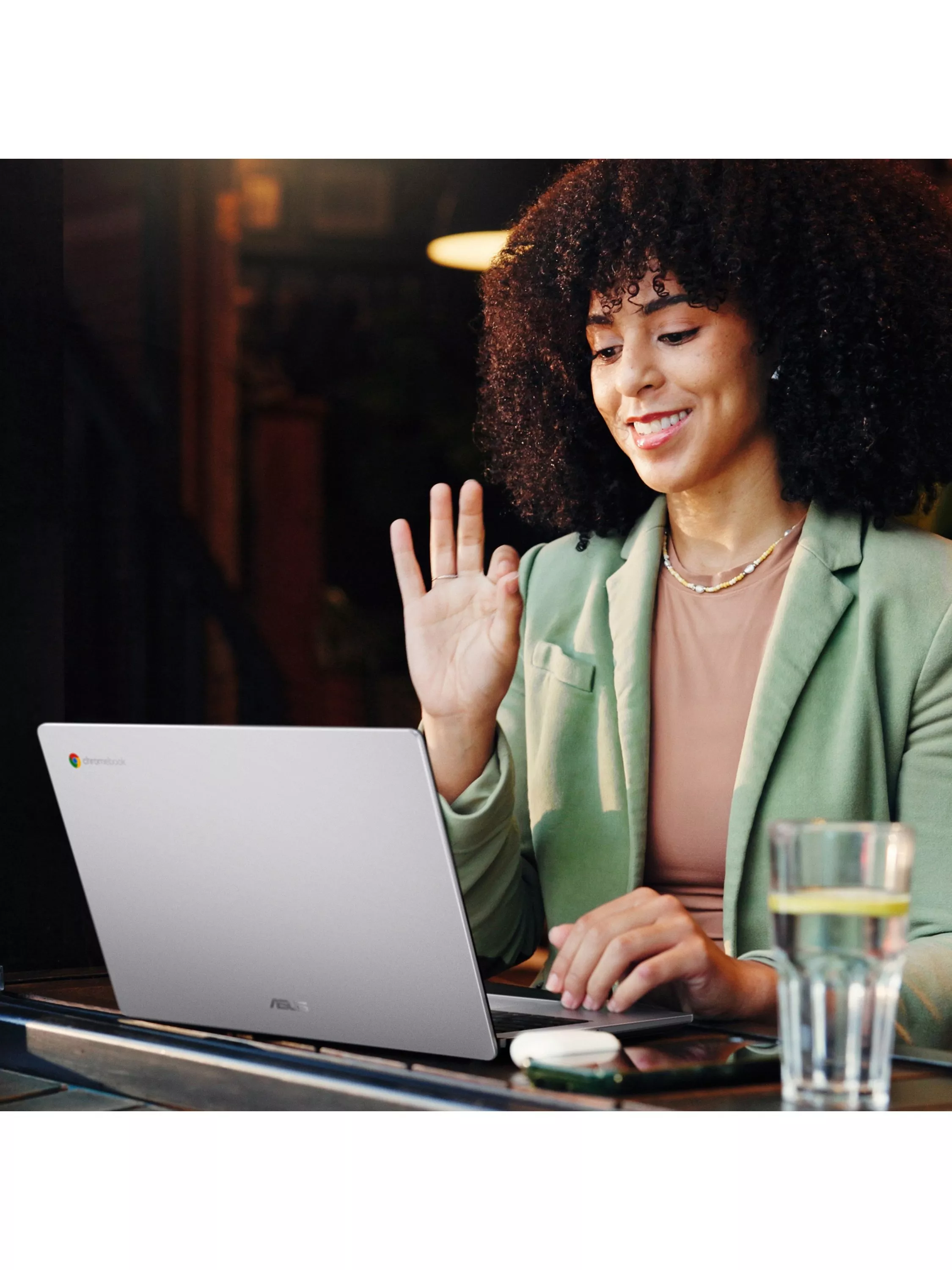Woman waving during a video call on laptop at a café table, remote work and online meeting concept