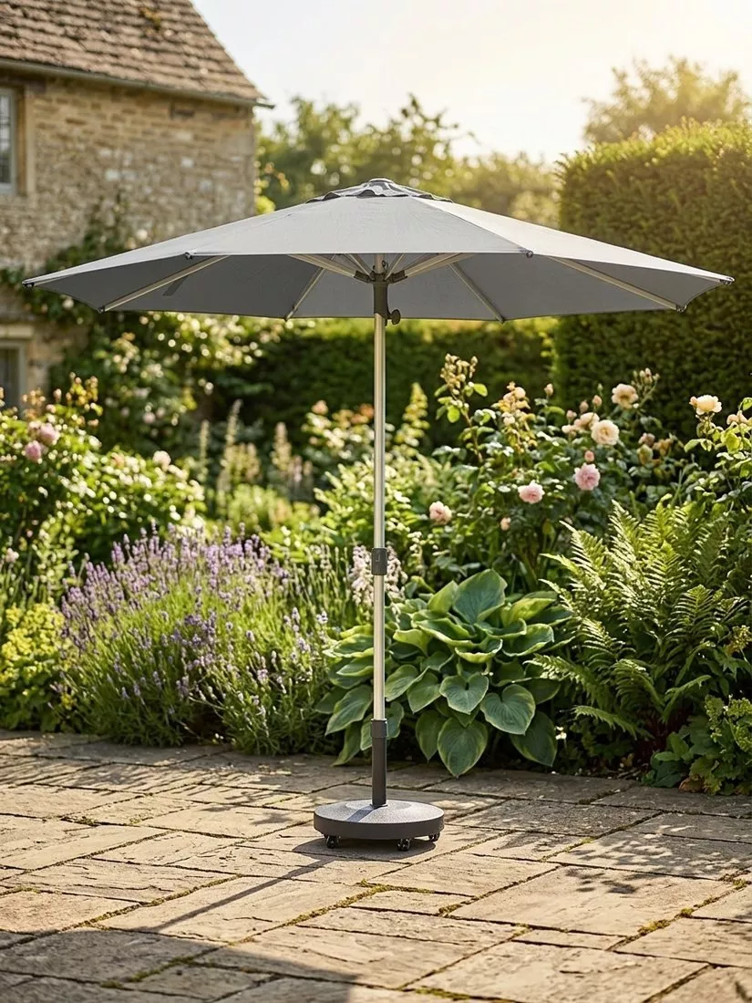 Grey garden parasol with sturdy base on stone patio, set in a lush cottage garden with flowers and greenery
