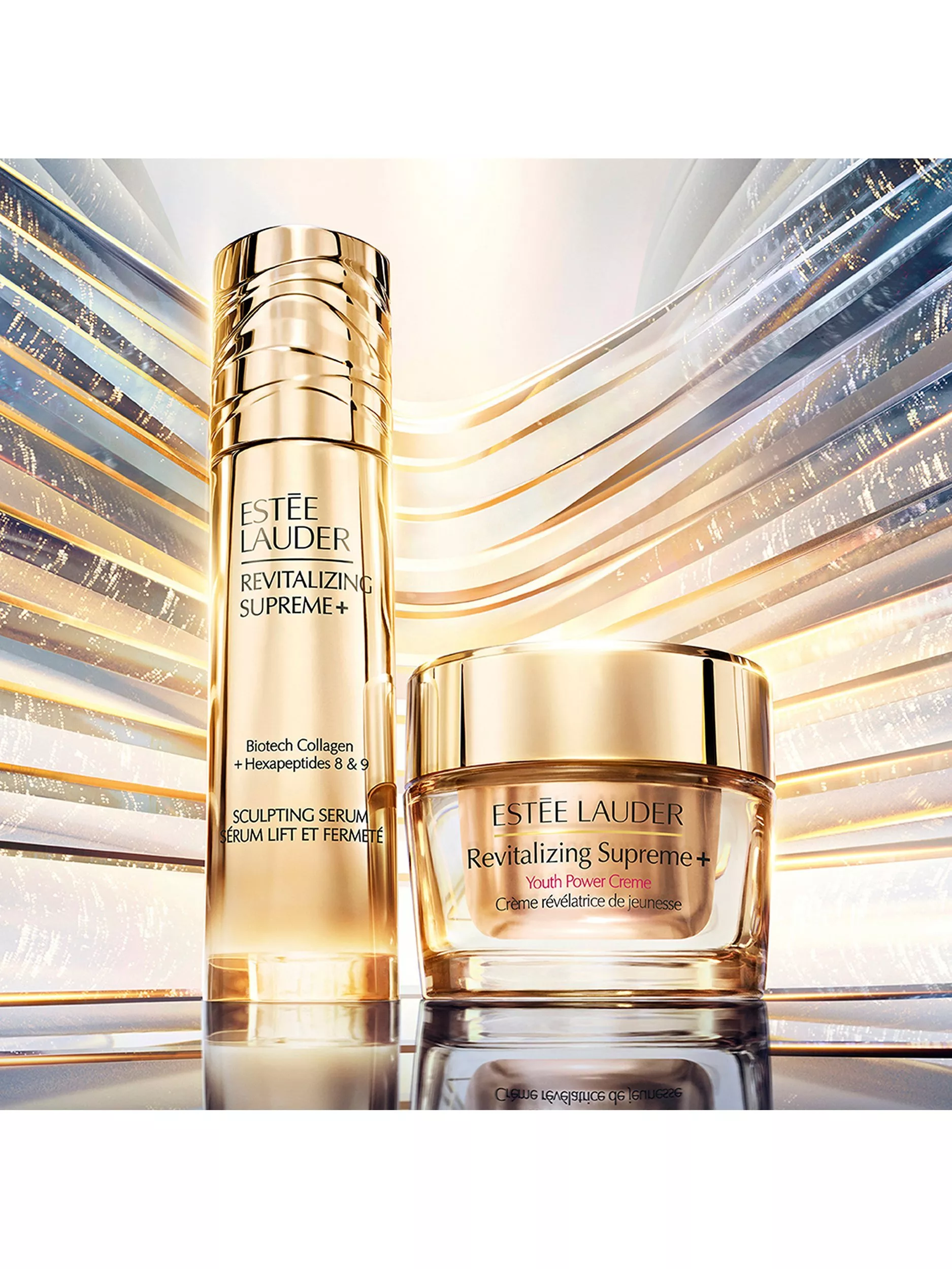 Estée Lauder Revitalizing Supreme+ serum and Youth Power Creme in gold packaging on luminous abstract backdrop