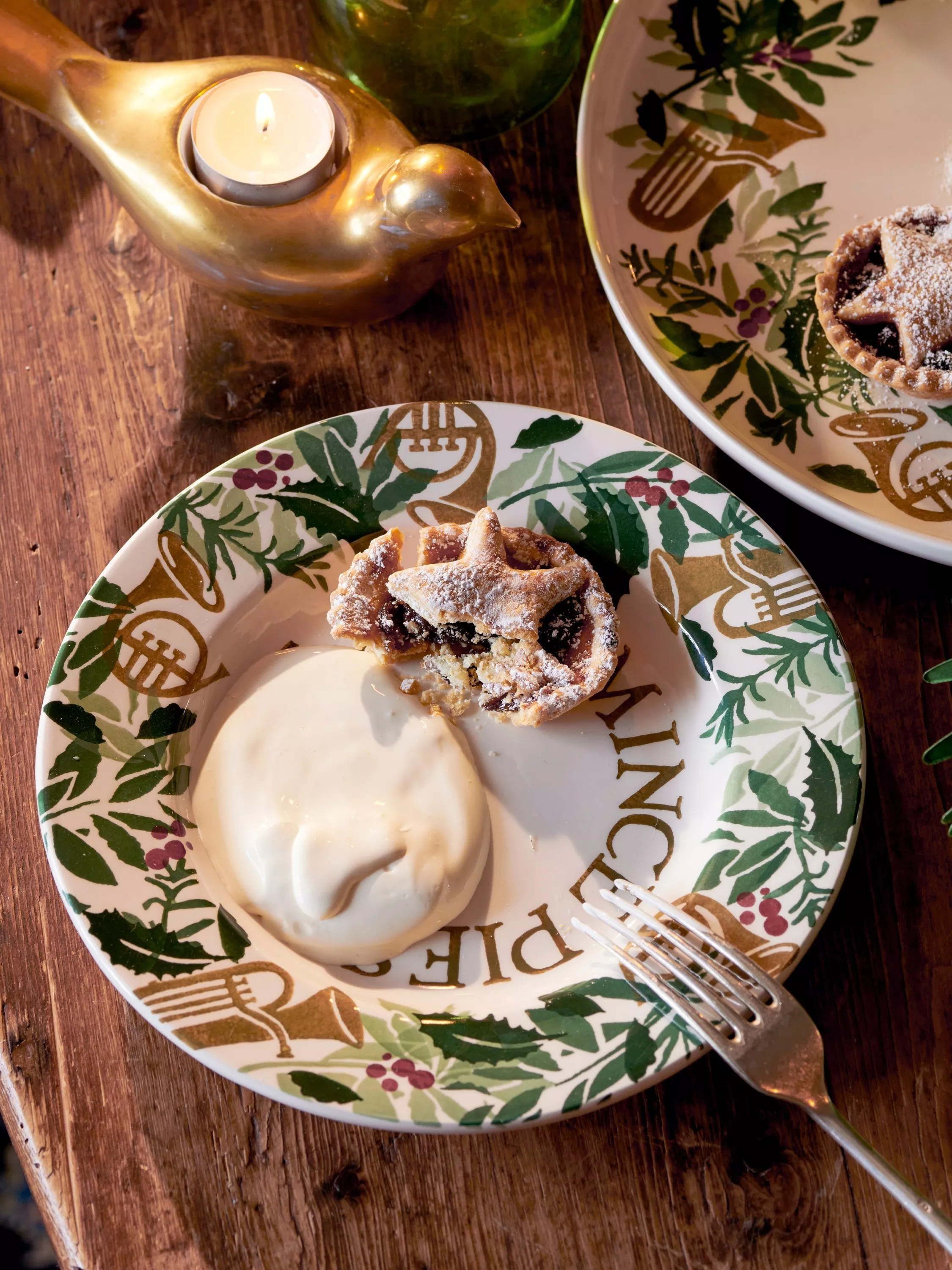 Mini mince pie with brandy cream on festive plate, beside brass bird candle holder on rustic table