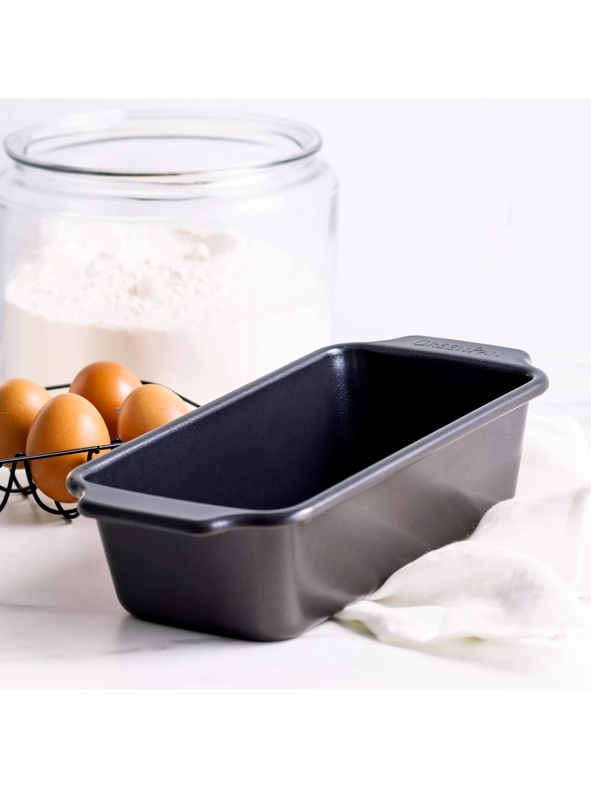 Non-stick loaf tin with eggs and flour on white surface, ideal for home baking bread and cake recipes
