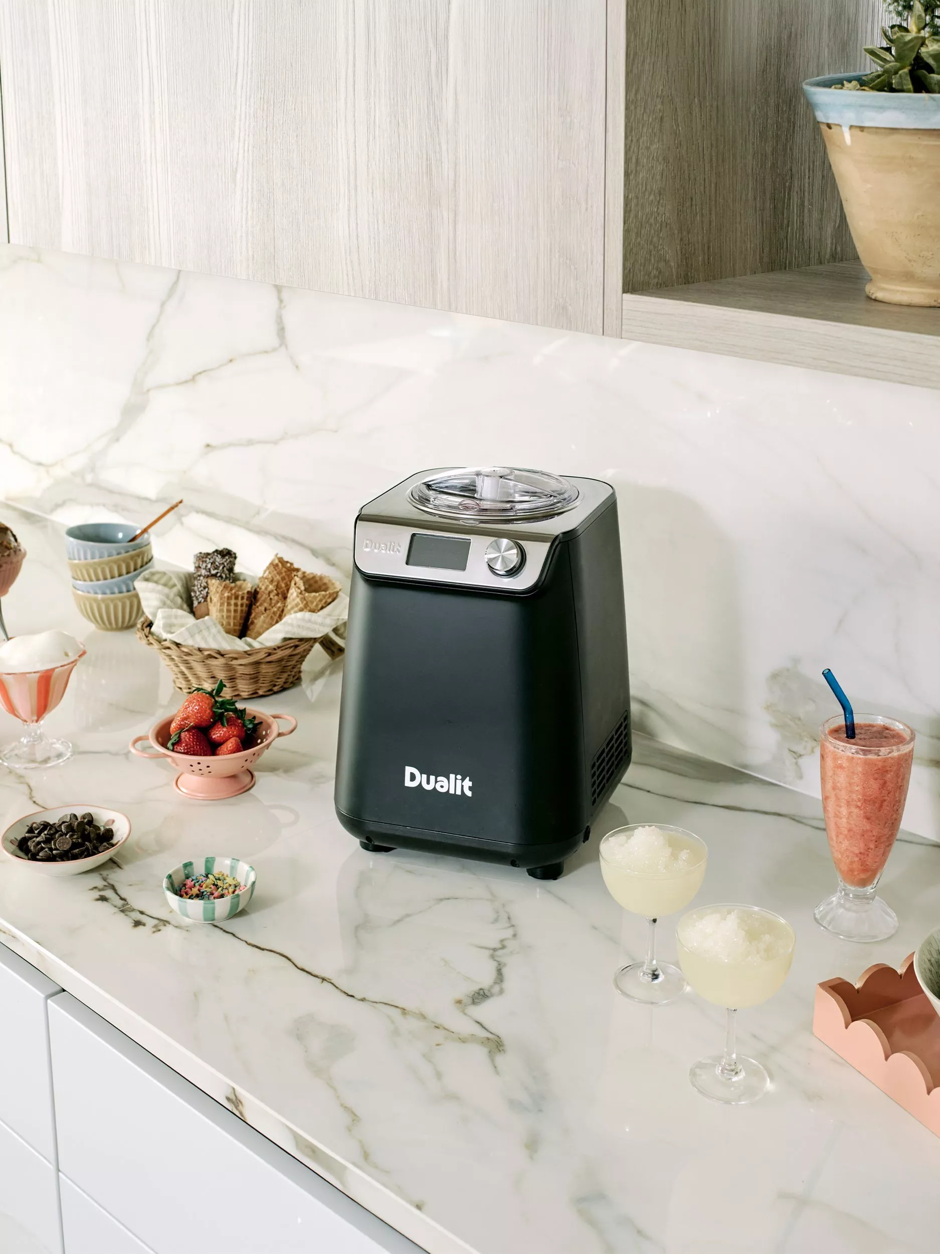 Dualit ice cream maker on marble kitchen worktop with waffle cones, strawberries, sprinkles and frozen cocktails
