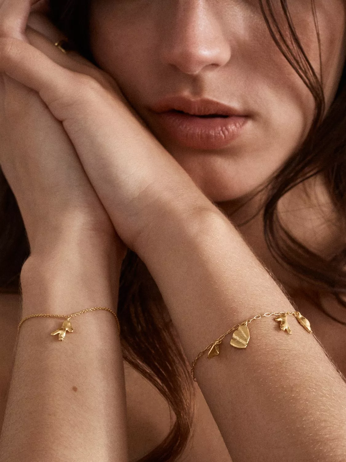 Close-up of woman wearing delicate gold charm bracelets, minimalist jewellery on wrists and hands near face