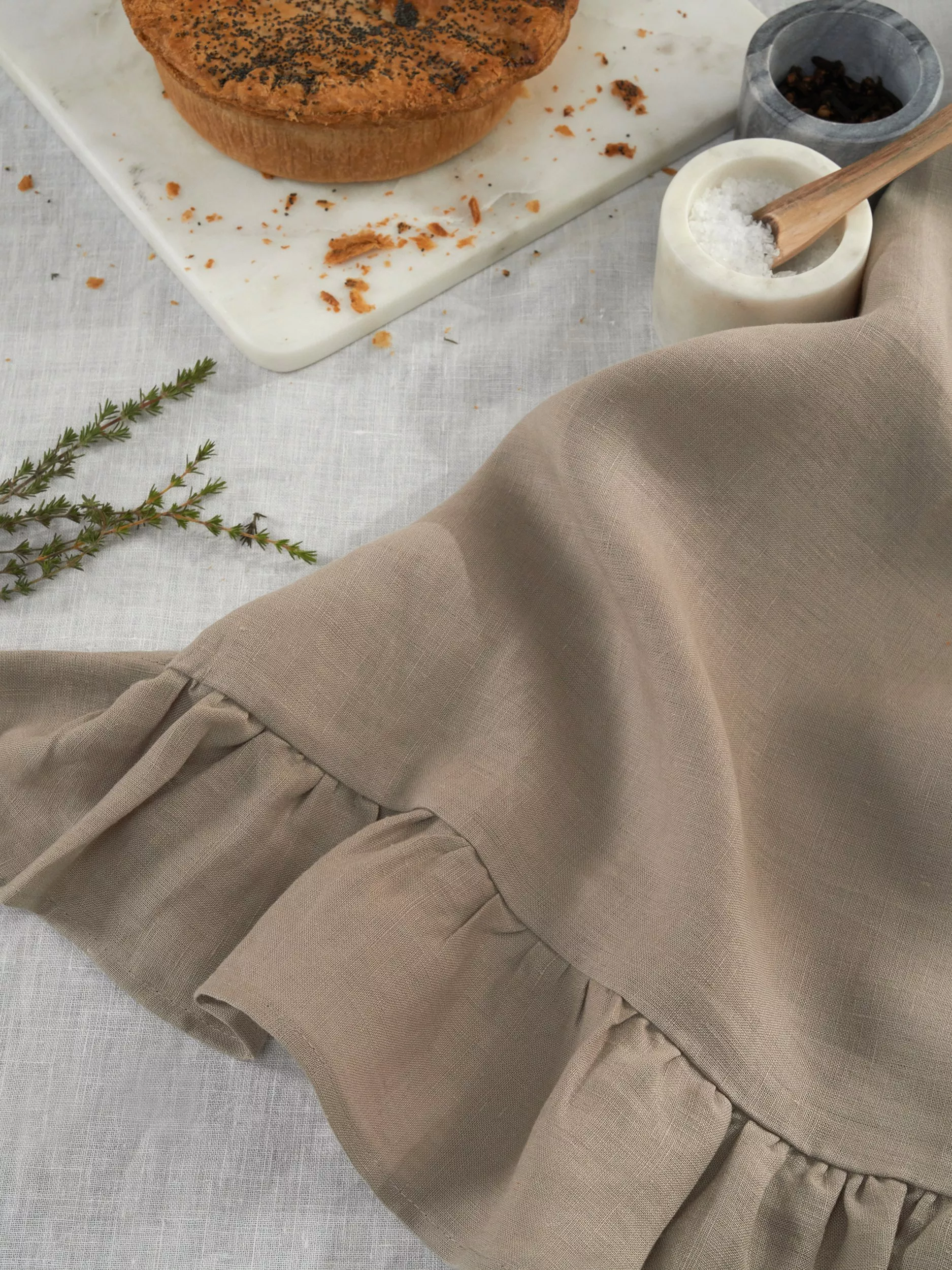 Taupe linen apron on kitchen table with pie, sea salt and herbs, rustic baking and cooking scene