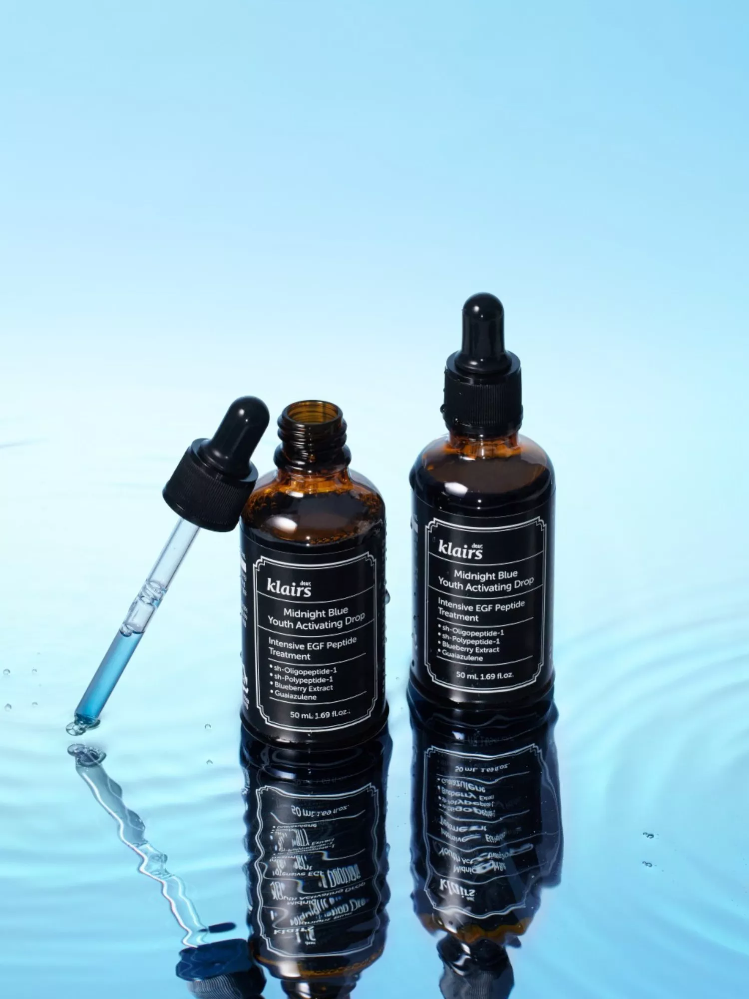 Klairs Midnight Blue Youth Activating Drop serum bottles with dropper pipette on reflective blue water surface