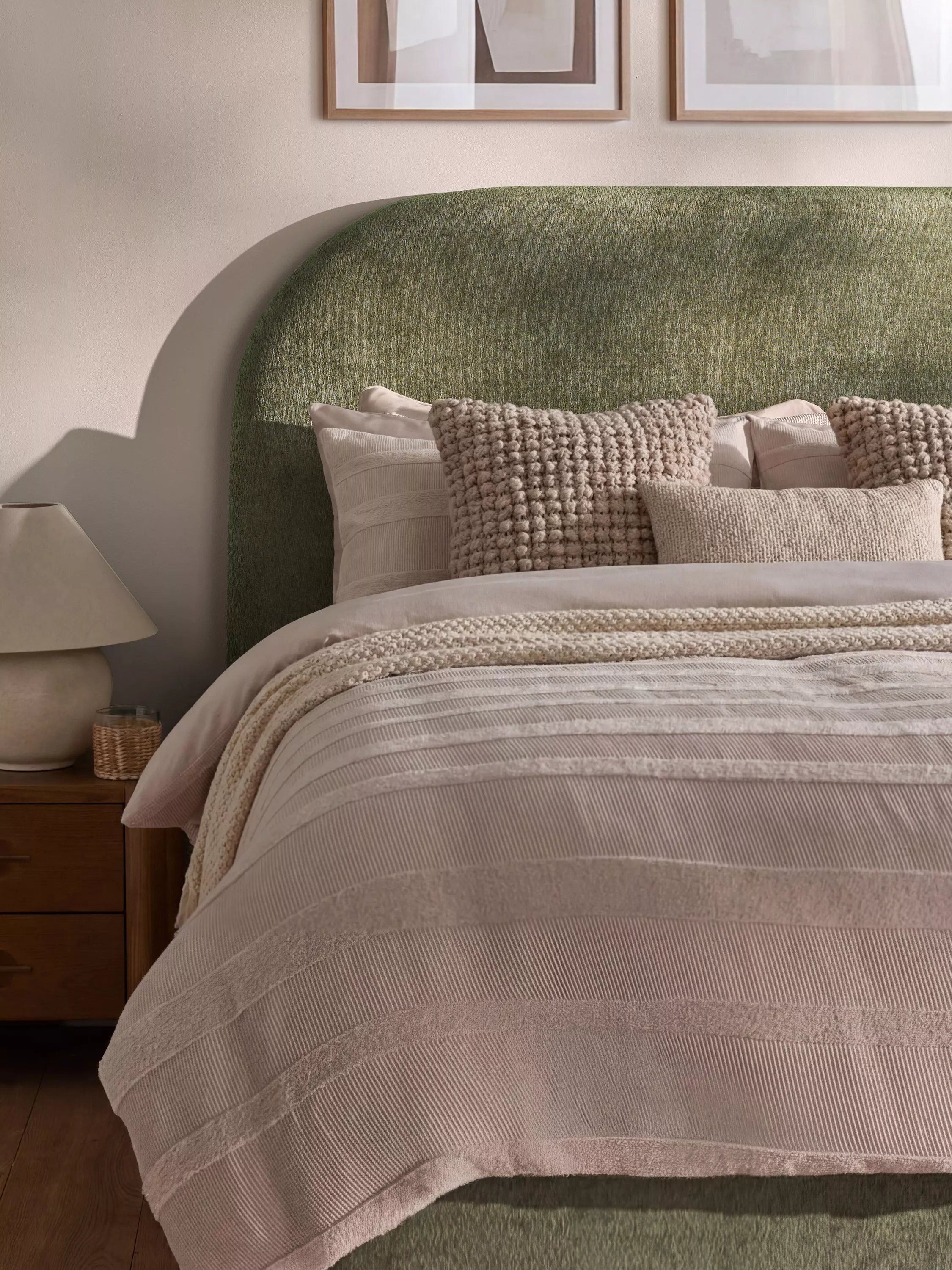 Cosy modern bedroom with green upholstered headboard, neutral bedding, textured cushions and bedside lamp
