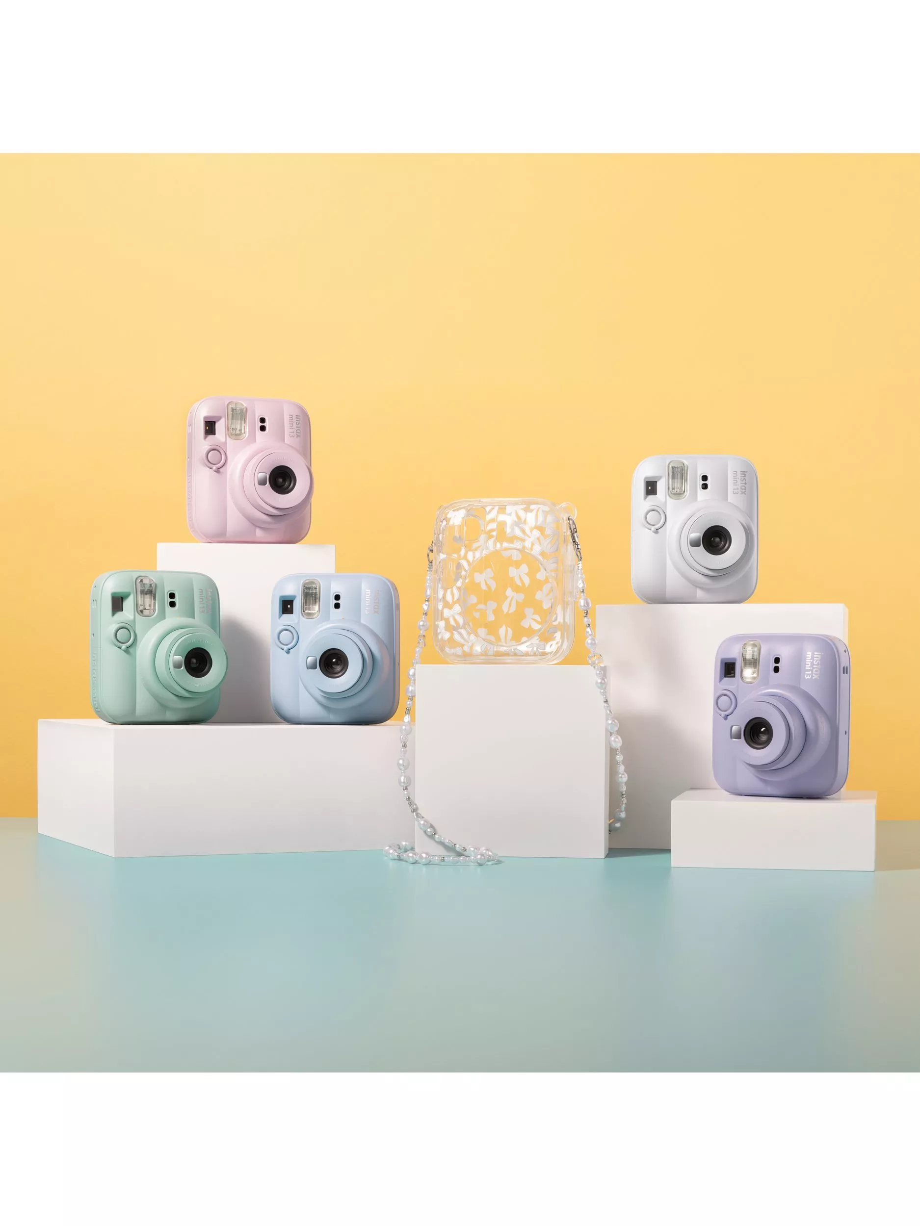 Pastel instant cameras on white display blocks with clear floral bag, studio product photo on yellow backdrop