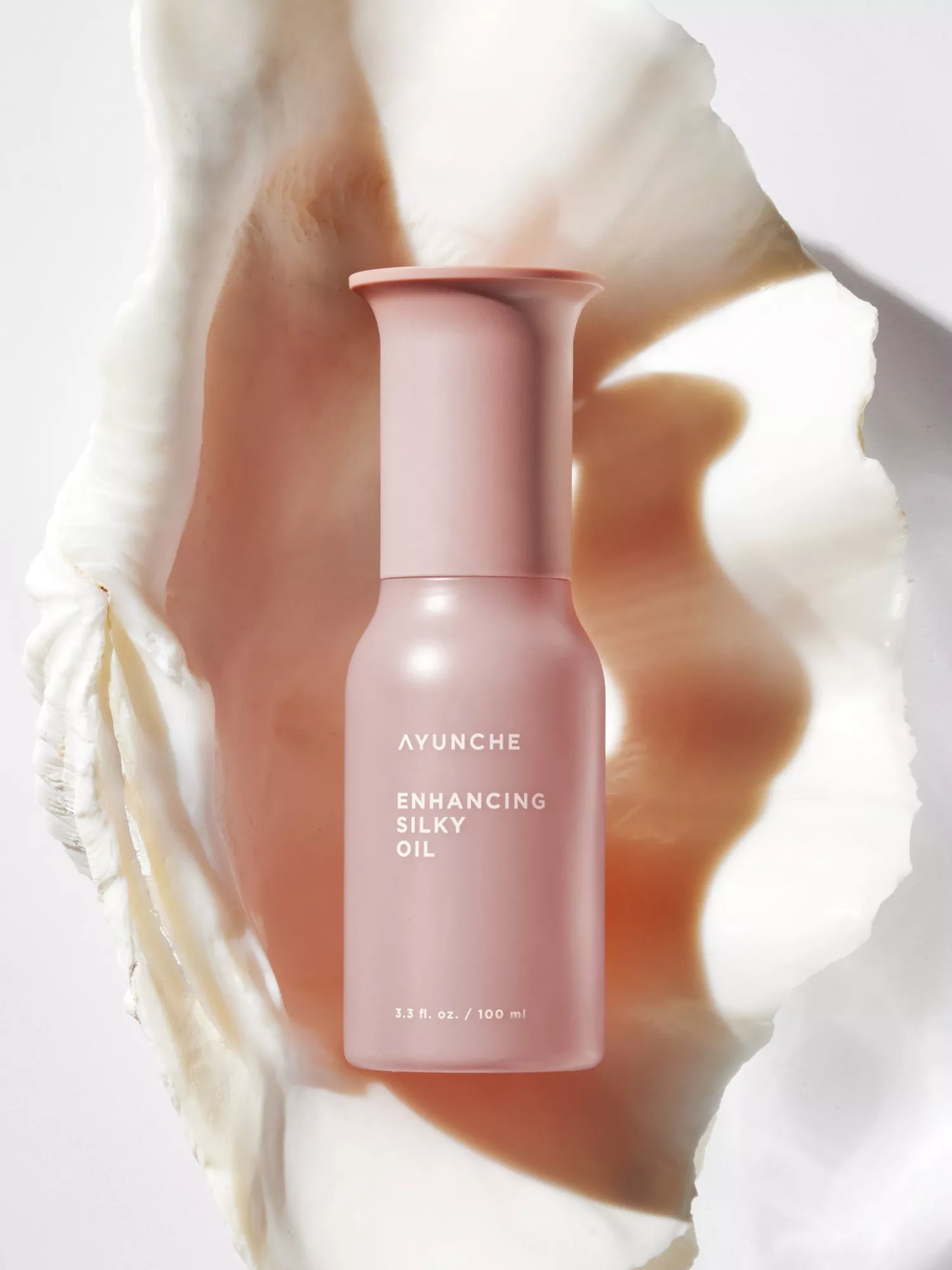 AYUNCHE Enhancing Silky Oil in pink 100 ml bottle, luxury hair oil product on pearlescent shell backdrop