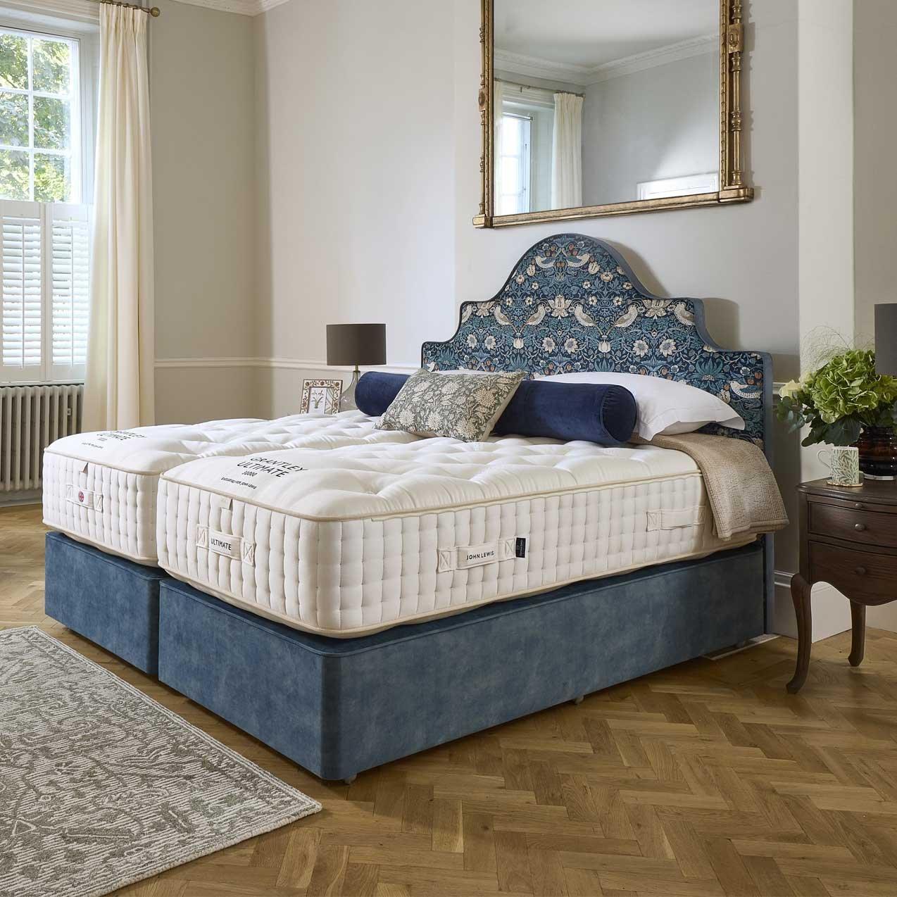 Luxury split-king bed with tufted mattresses, a blue upholstered base, and a matching patterned arched headboard in a bright bedroom.