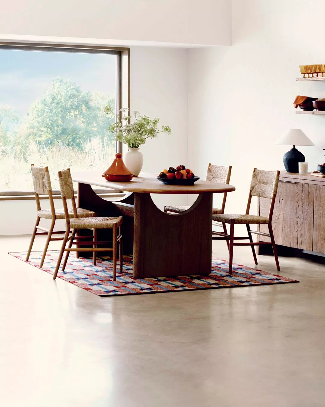 Modern dining room with wooden table, woven chairs, patterned rug and large window with garden view