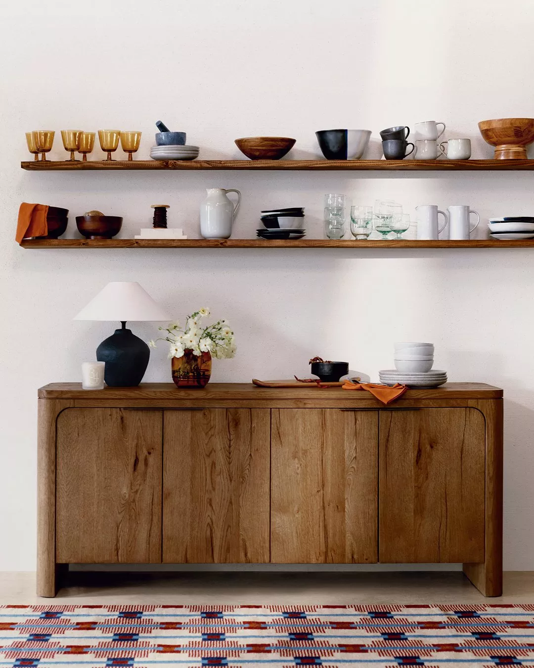 Minimalist dining room with wooden sideboard, open shelves and ceramic tableware on white wall background