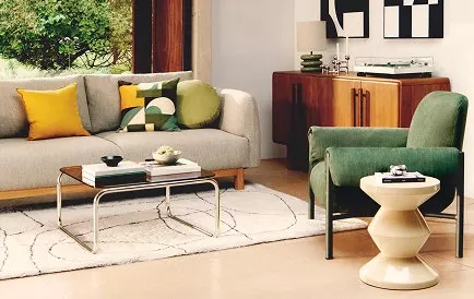 Modern living room with large windows, grey sofa, green armchair, stylish decor, and a mounted TV screen.