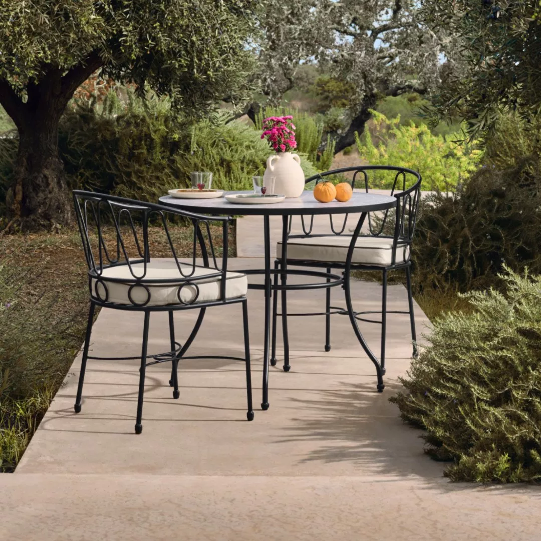 Striped outdoor lounge chairs and side table on patio, with garden plants, fruit bowl and watering can