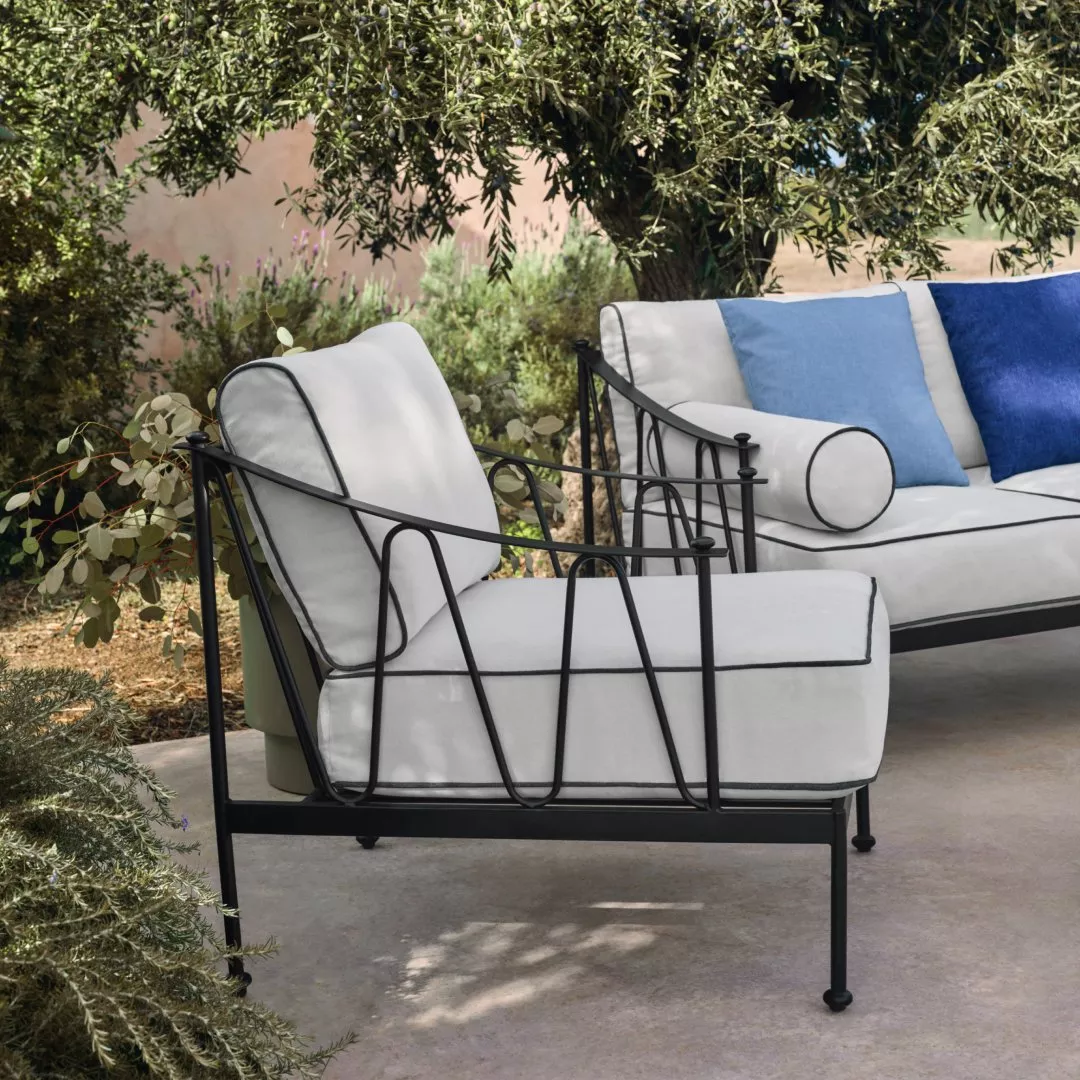 Stylish outdoor seating with black metal frames and white cushions under a lush tree in a serene garden setting.