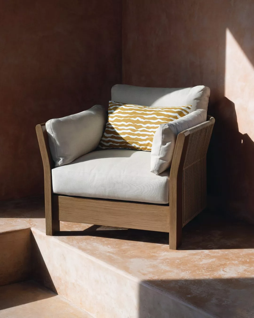 Modern outdoor lounge chair with beige cushions and yellow striped pillow in sunlit patio corner