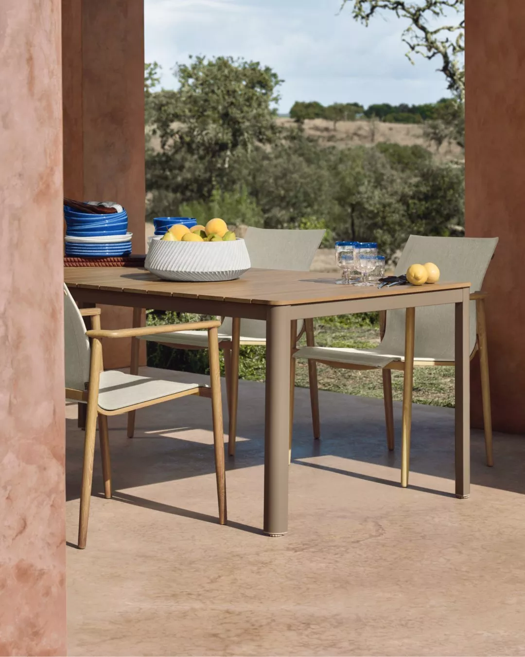Outdoor dining area with a wooden table set for a meal, overlooking a scenic landscape under a cloudy sky.