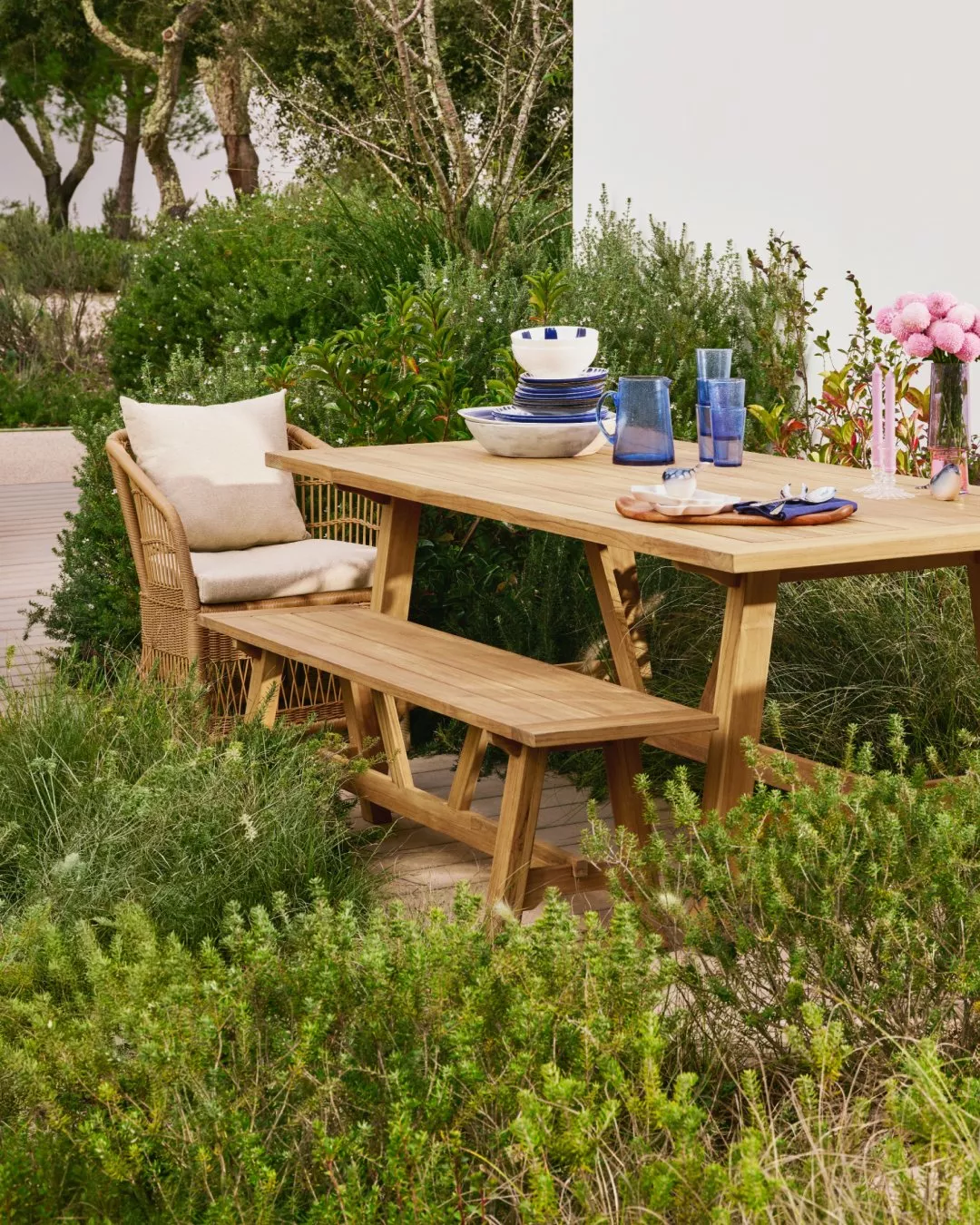 Ceramic dishes in blue and white patterns on a wooden table with utensils and mini cups.