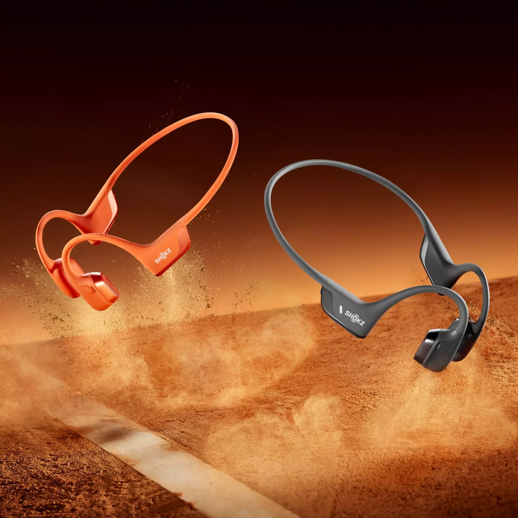 Shokz bone conduction sports headphones in orange and grey, floating over dusty running track background