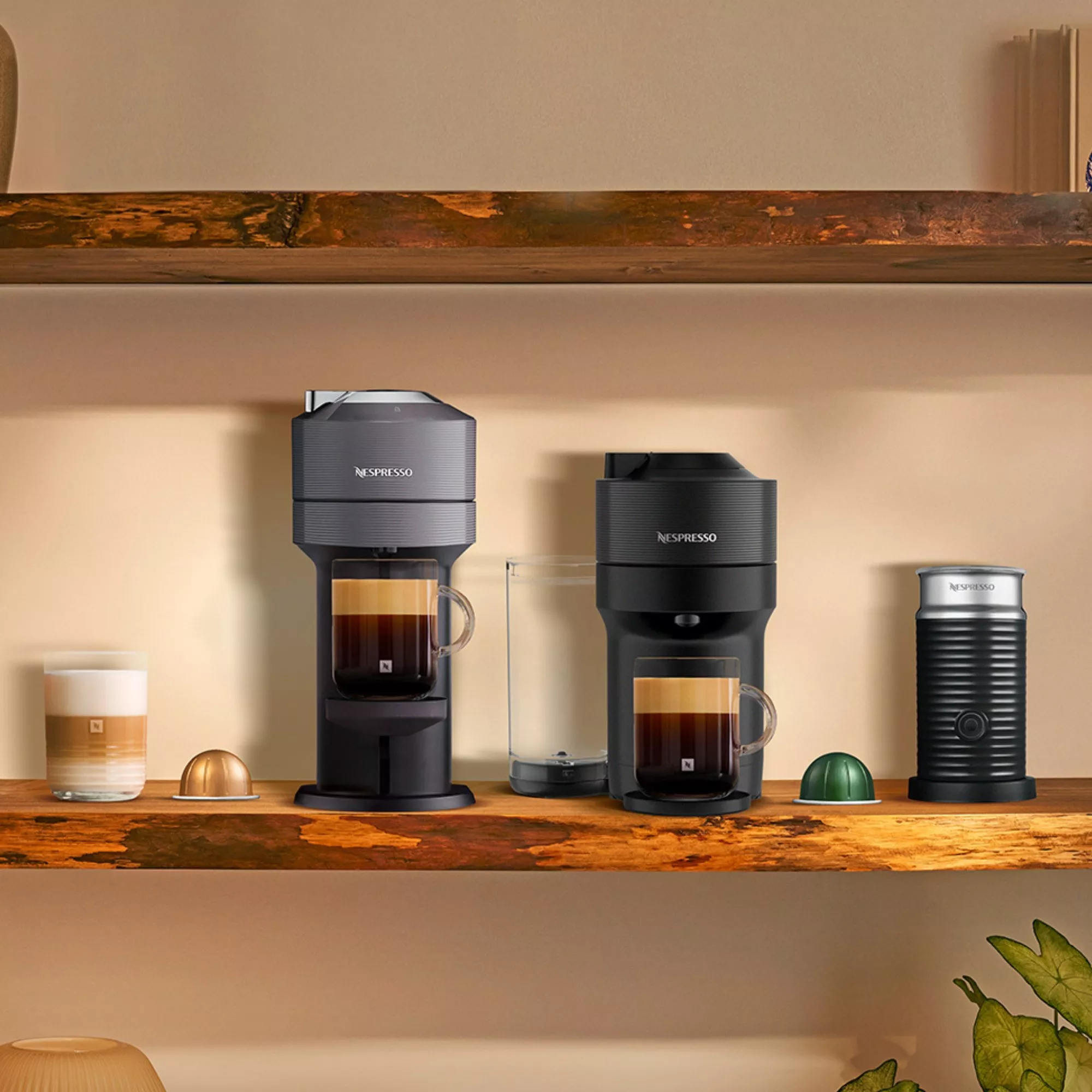 Two coffee machines on a shelf with a milk frother and coffee in glasses next to them 