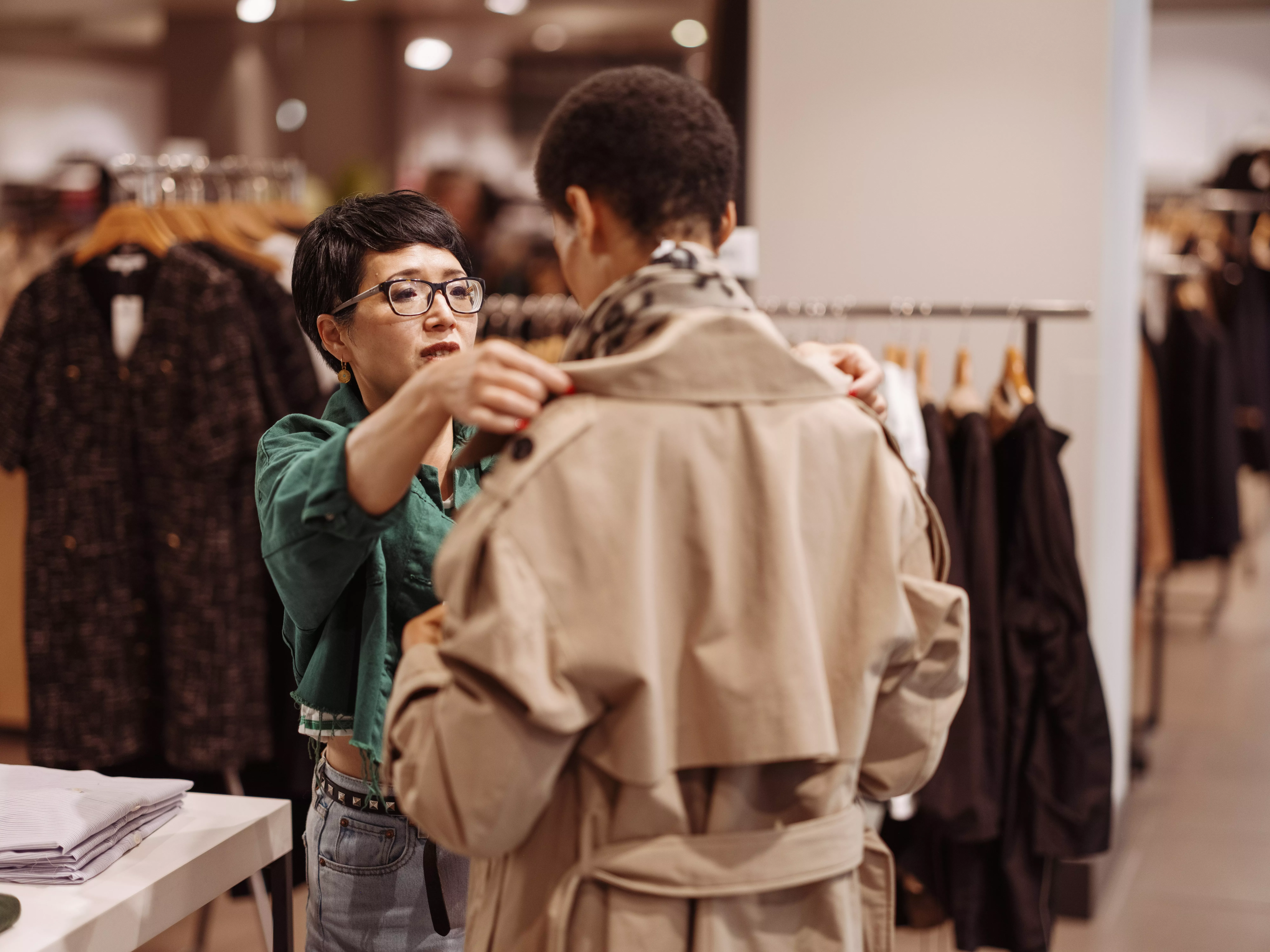stylist in store helping a customer try on a coat