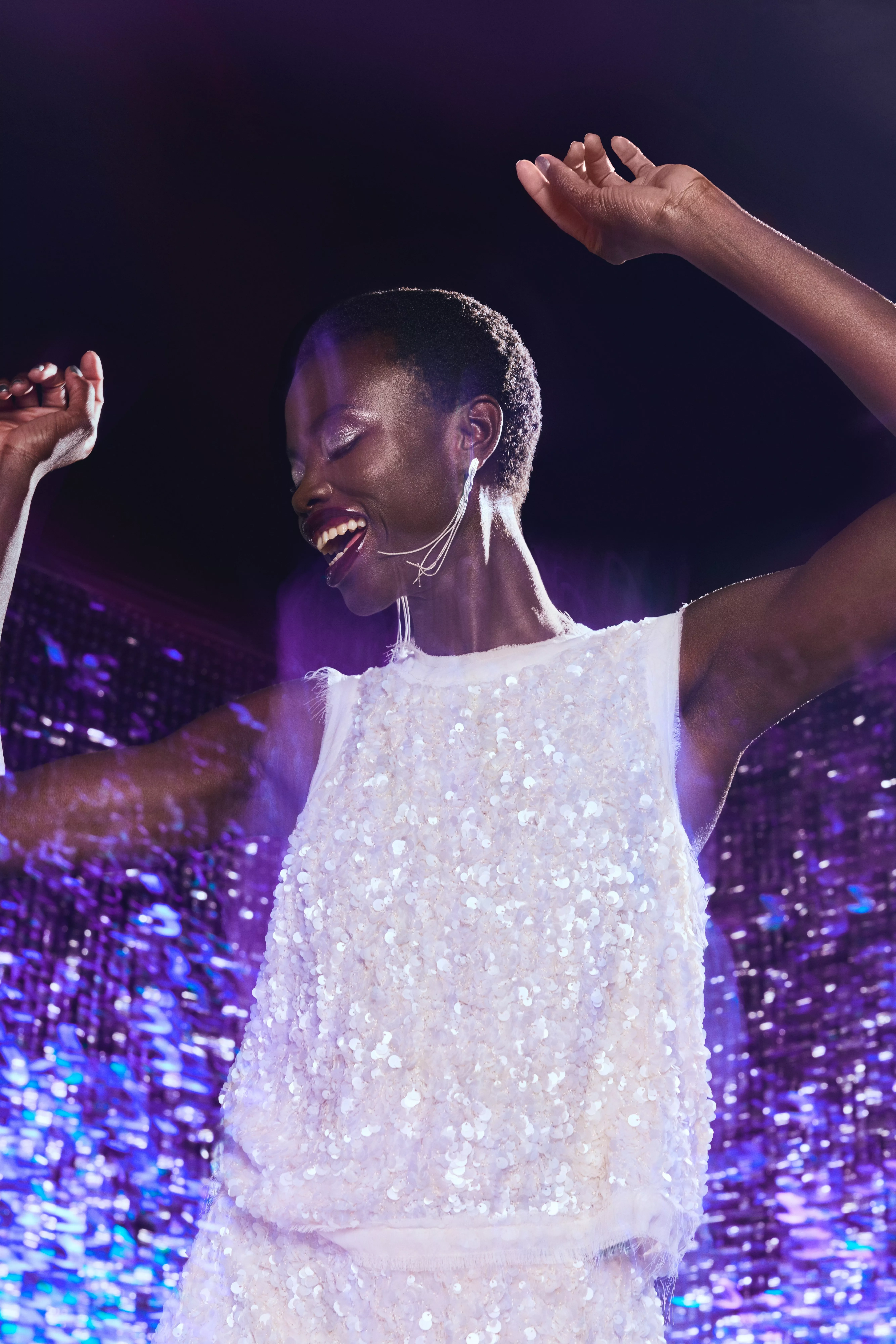 Woman wearing a white sequin dress dancing in front of a sparkly background