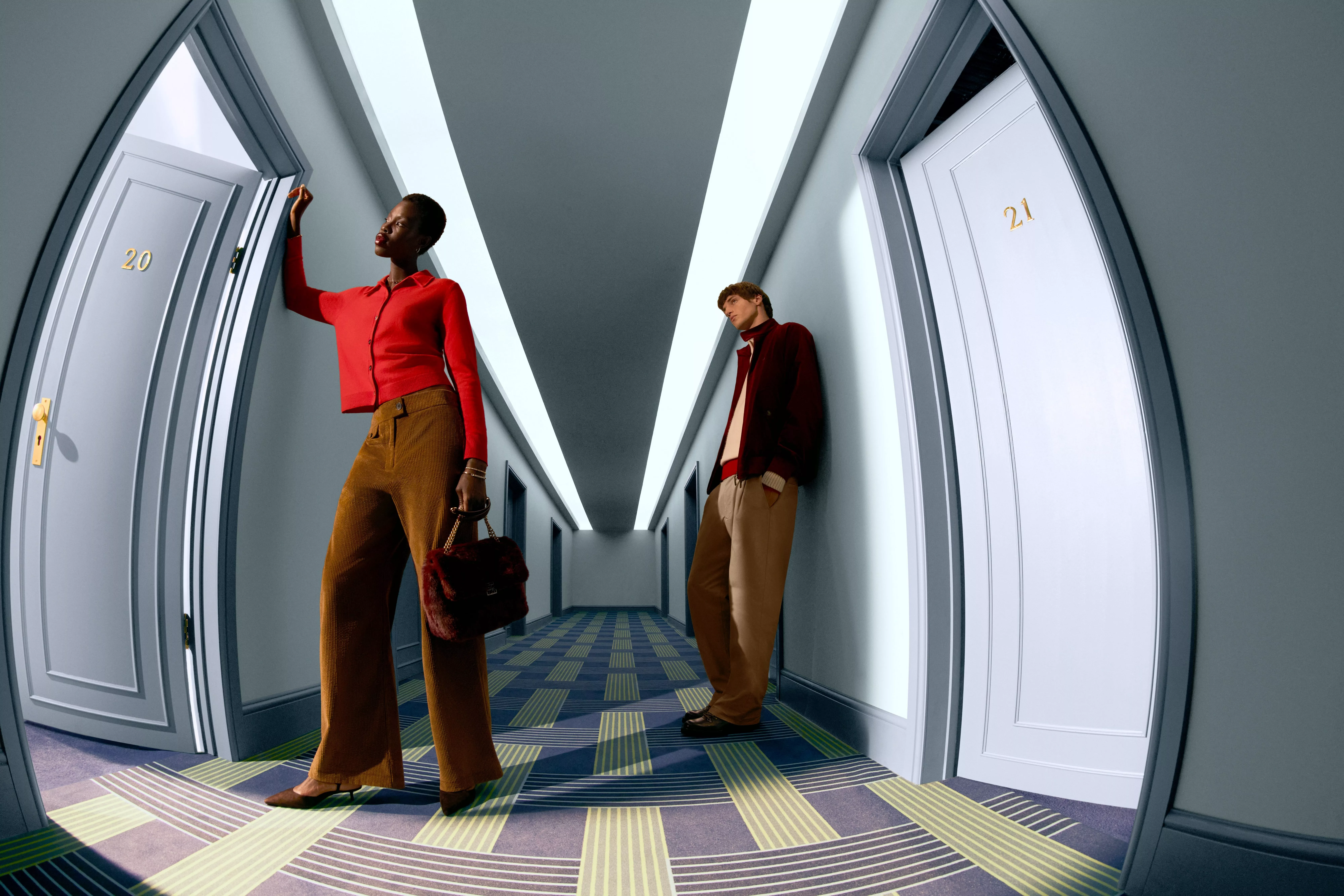 Man standing in a corridor wearing tan chinos and a brown jacket