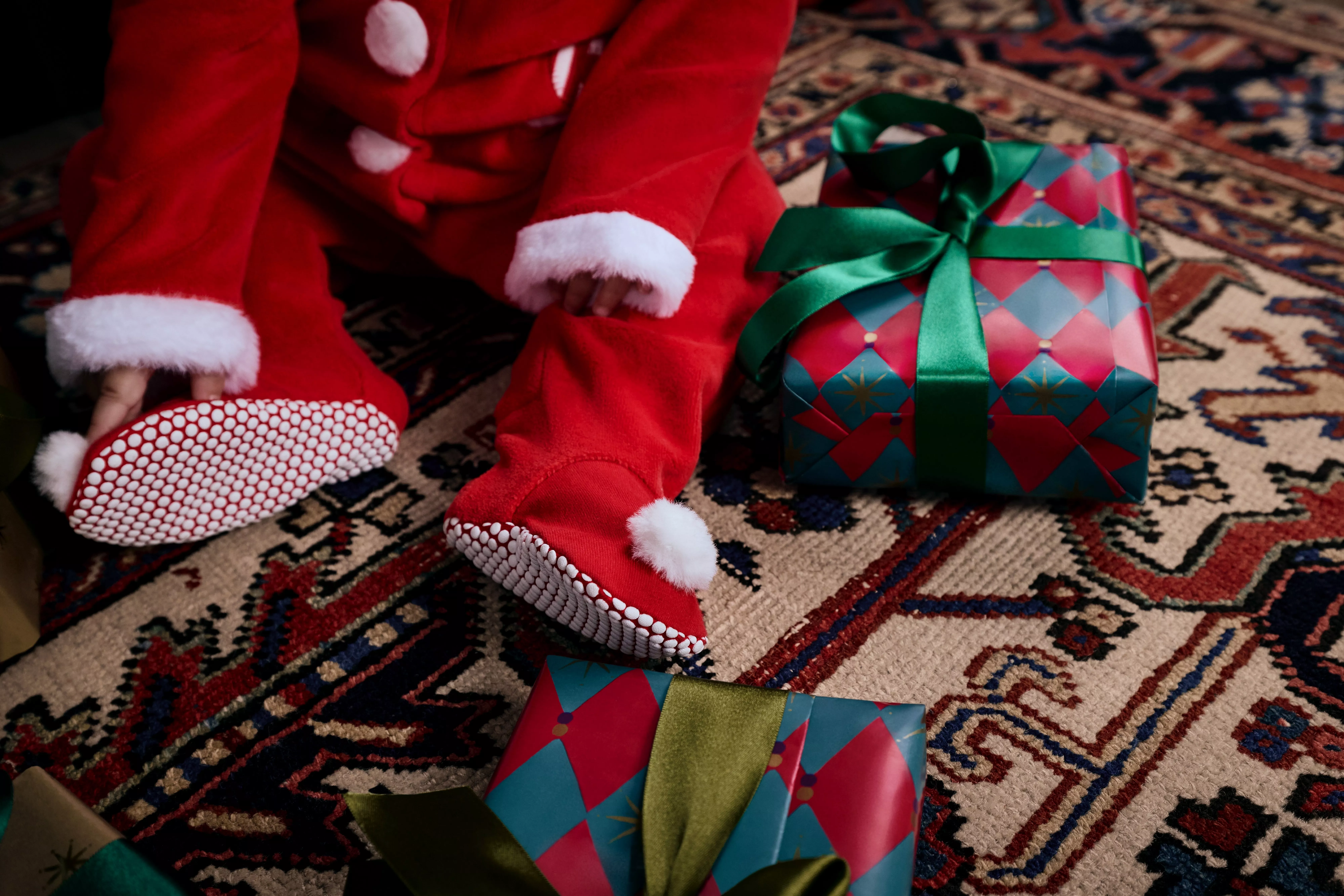 A baby sitting in a santa onesie with wrapped gifts