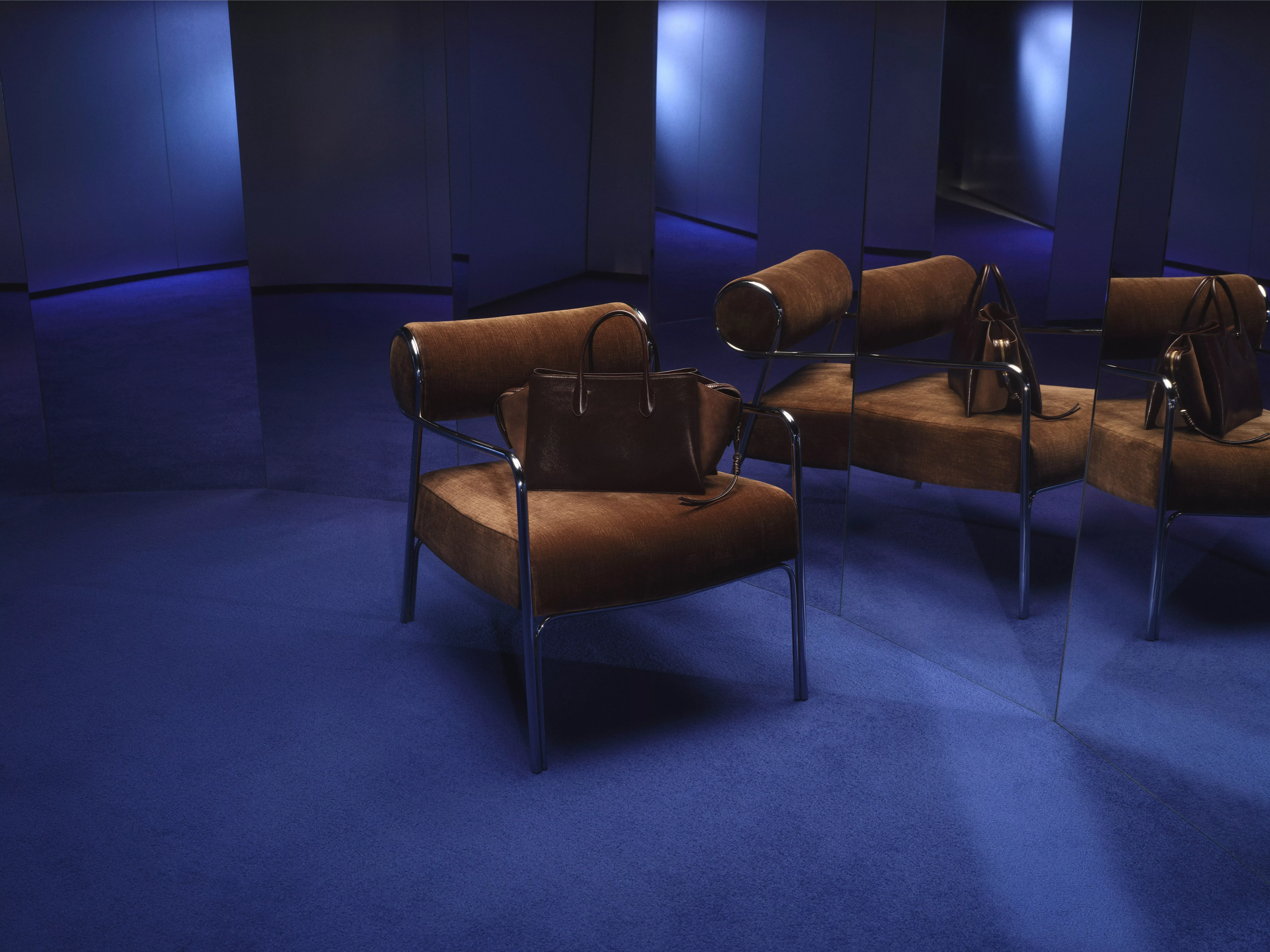 A brown velvet chair on a blue carpet with a brown suede handbag on the seat
