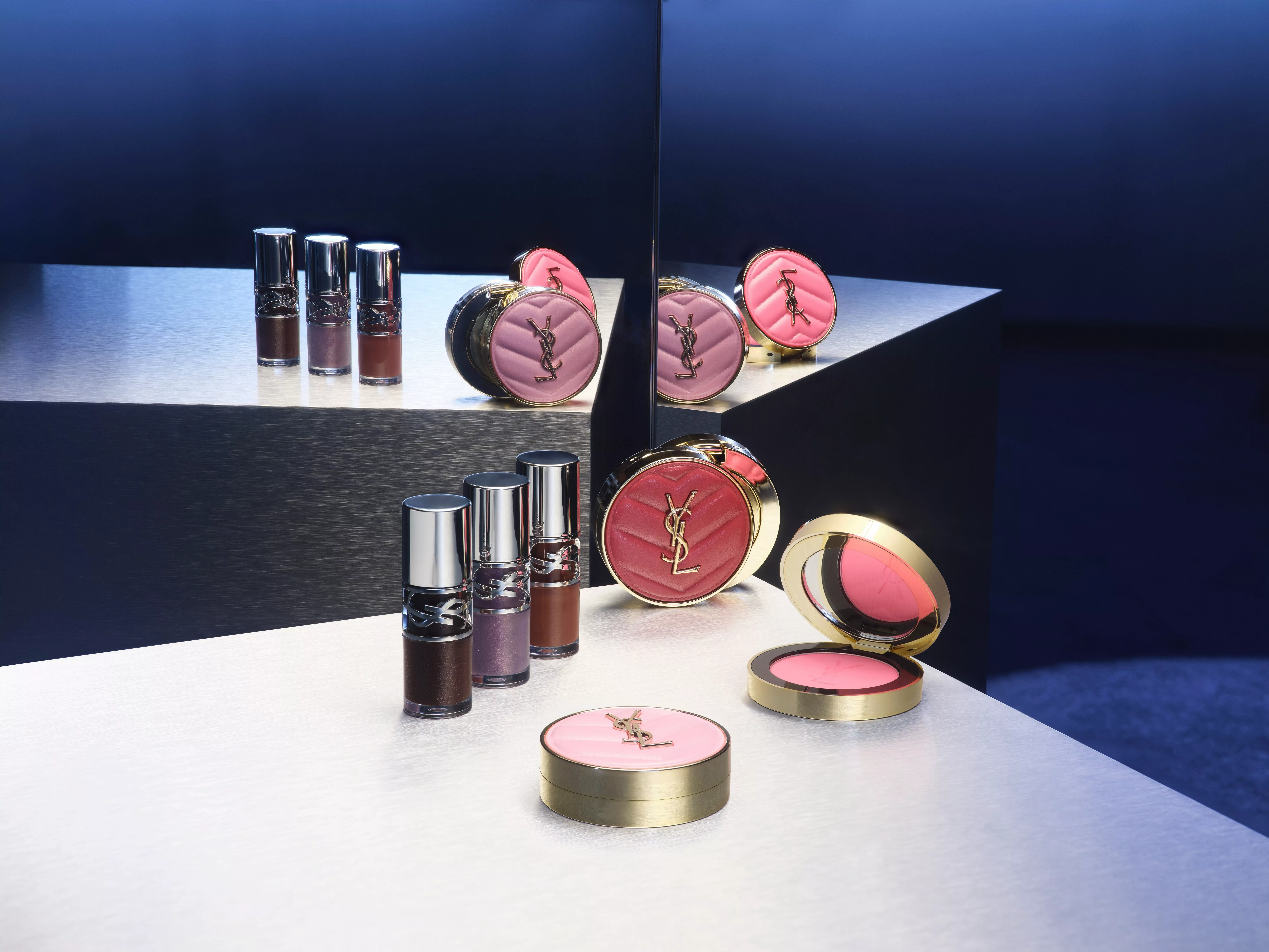 In the center, YSL lipsticks and pink quilted compacts are arranged against a blue background.