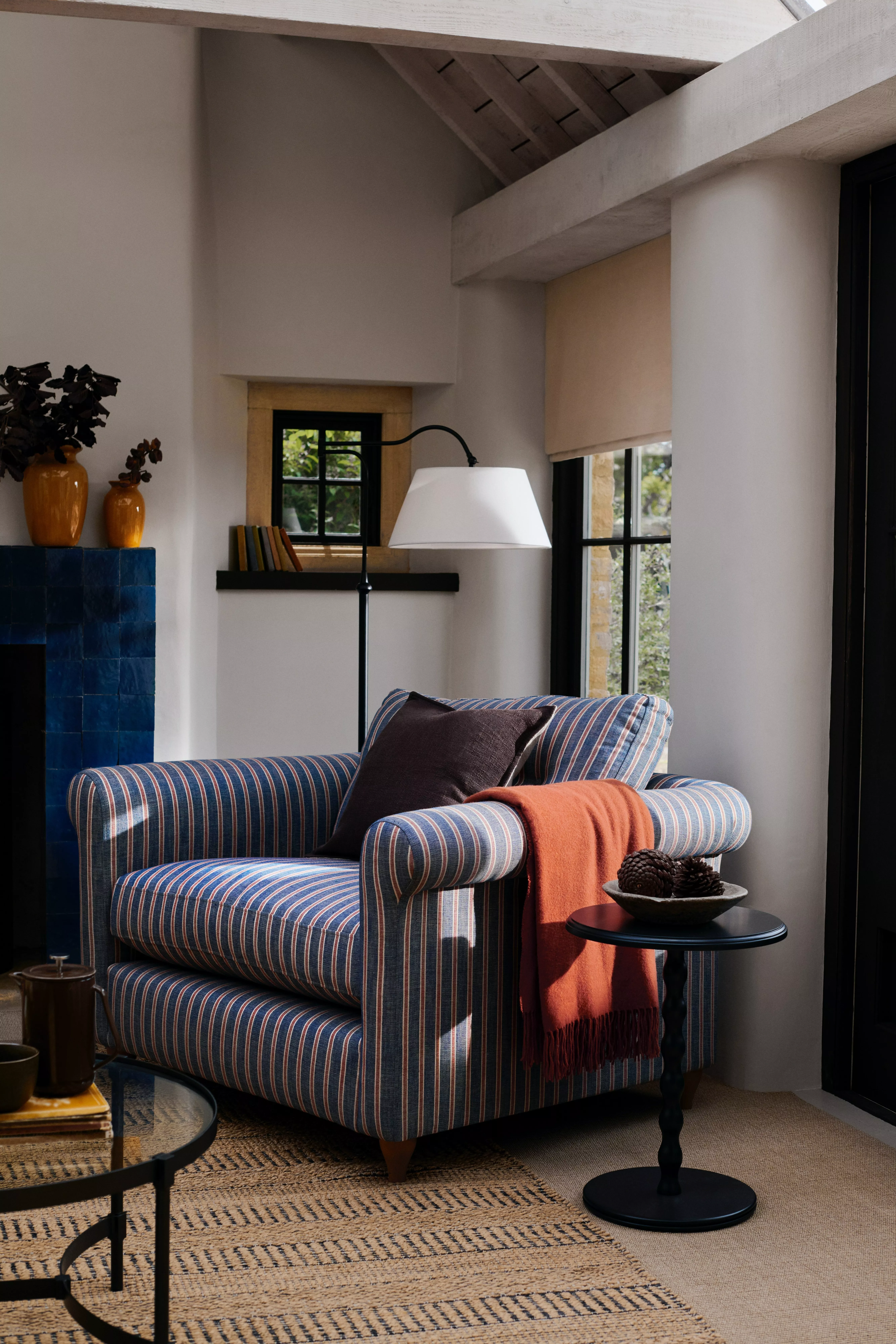 Striped upholstered armchair with orange throw, side table and floor lamp in a cosy modern living room