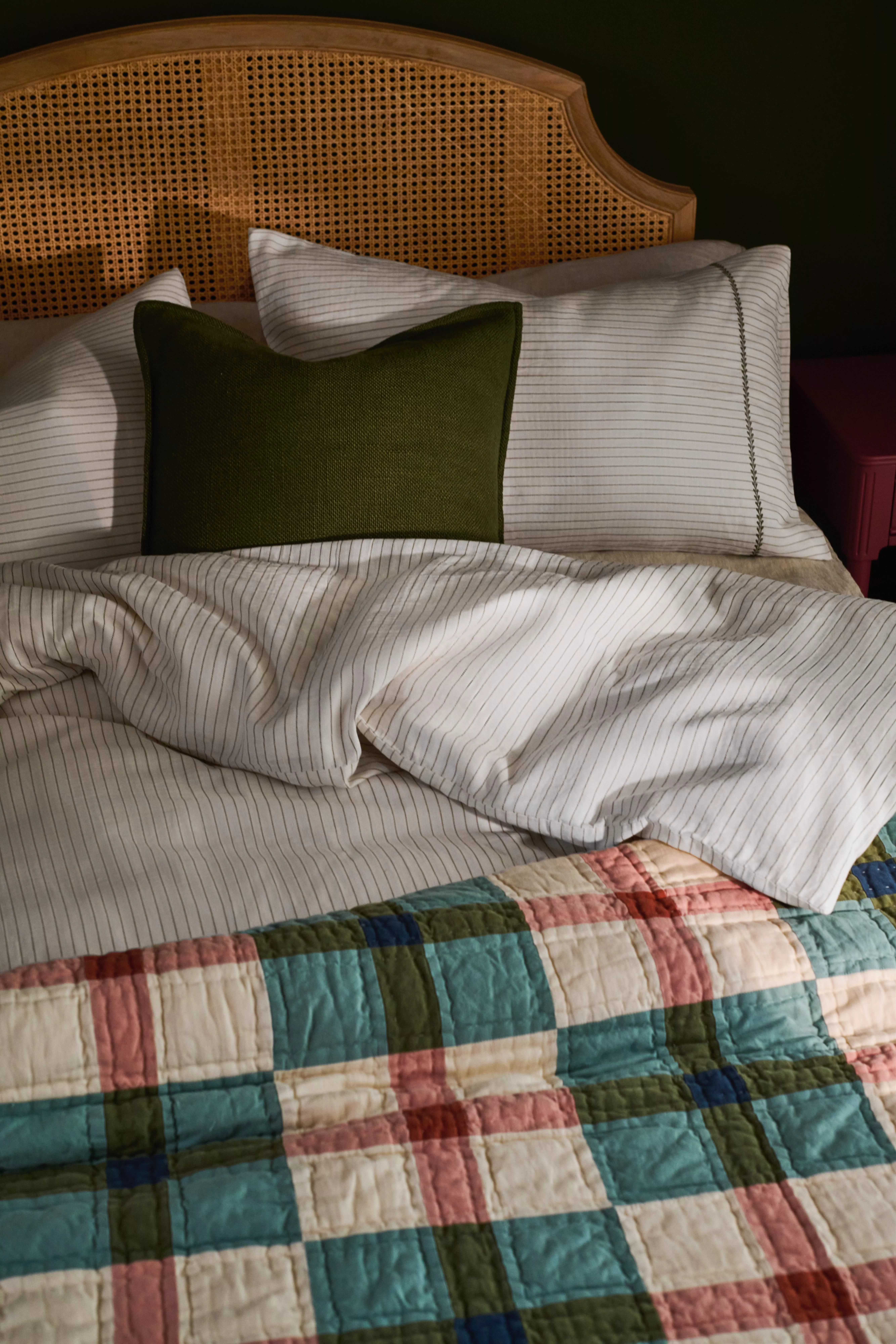 Rattan bed frame with green and white quilt with red beside tables and lamps