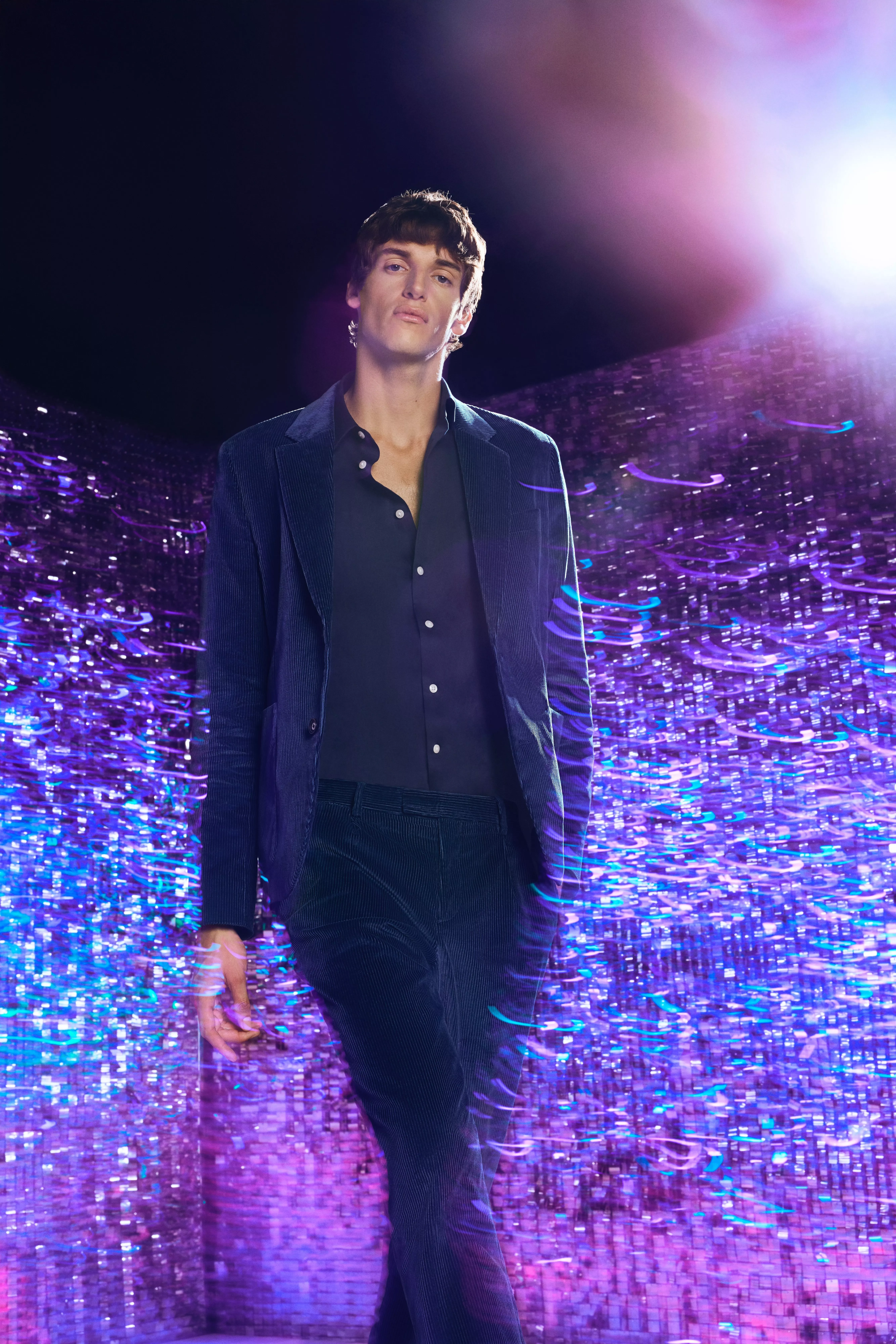 Man in a navy velvet suit standing in front of a sparkly background