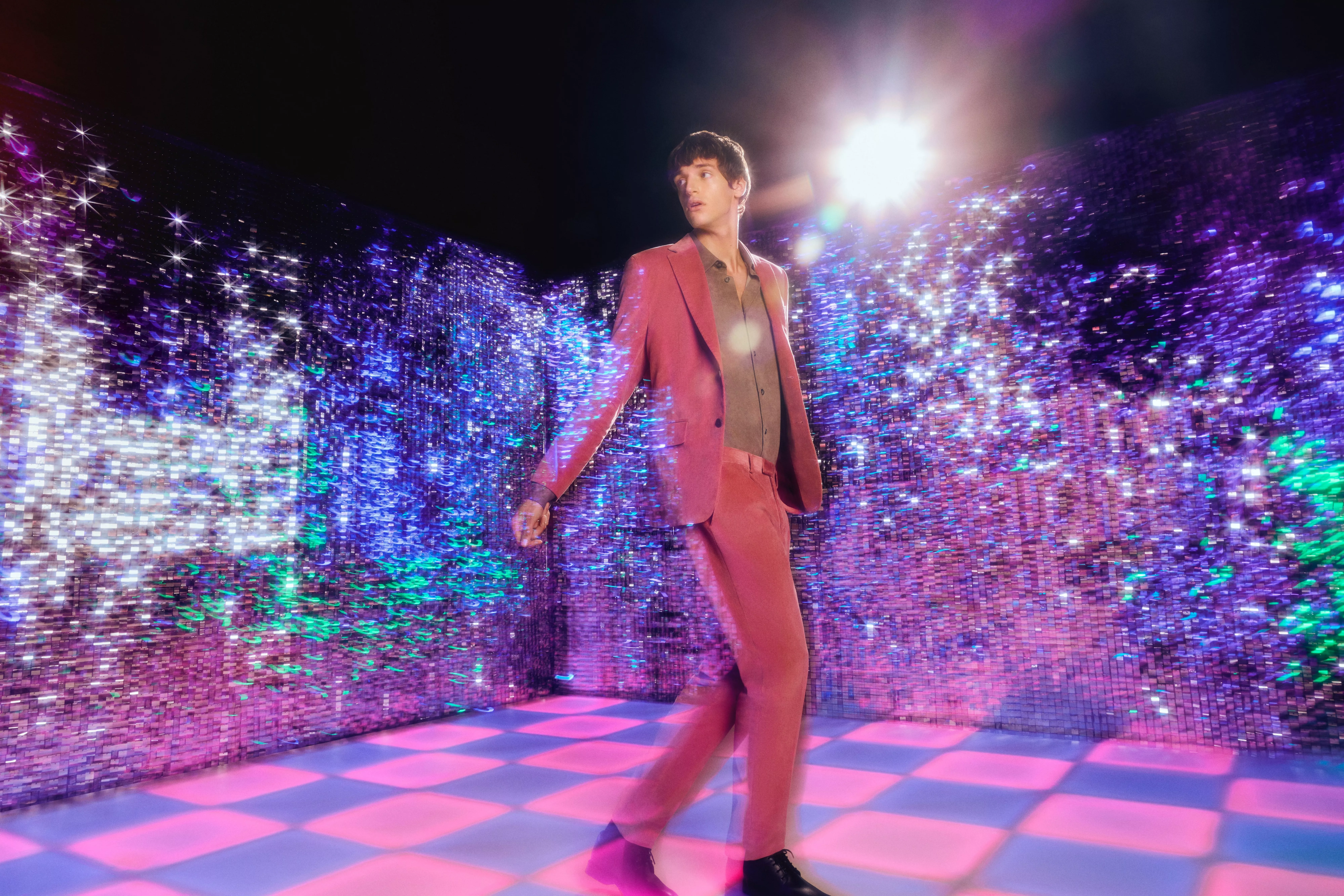 man wearing pink suit standing against disco background