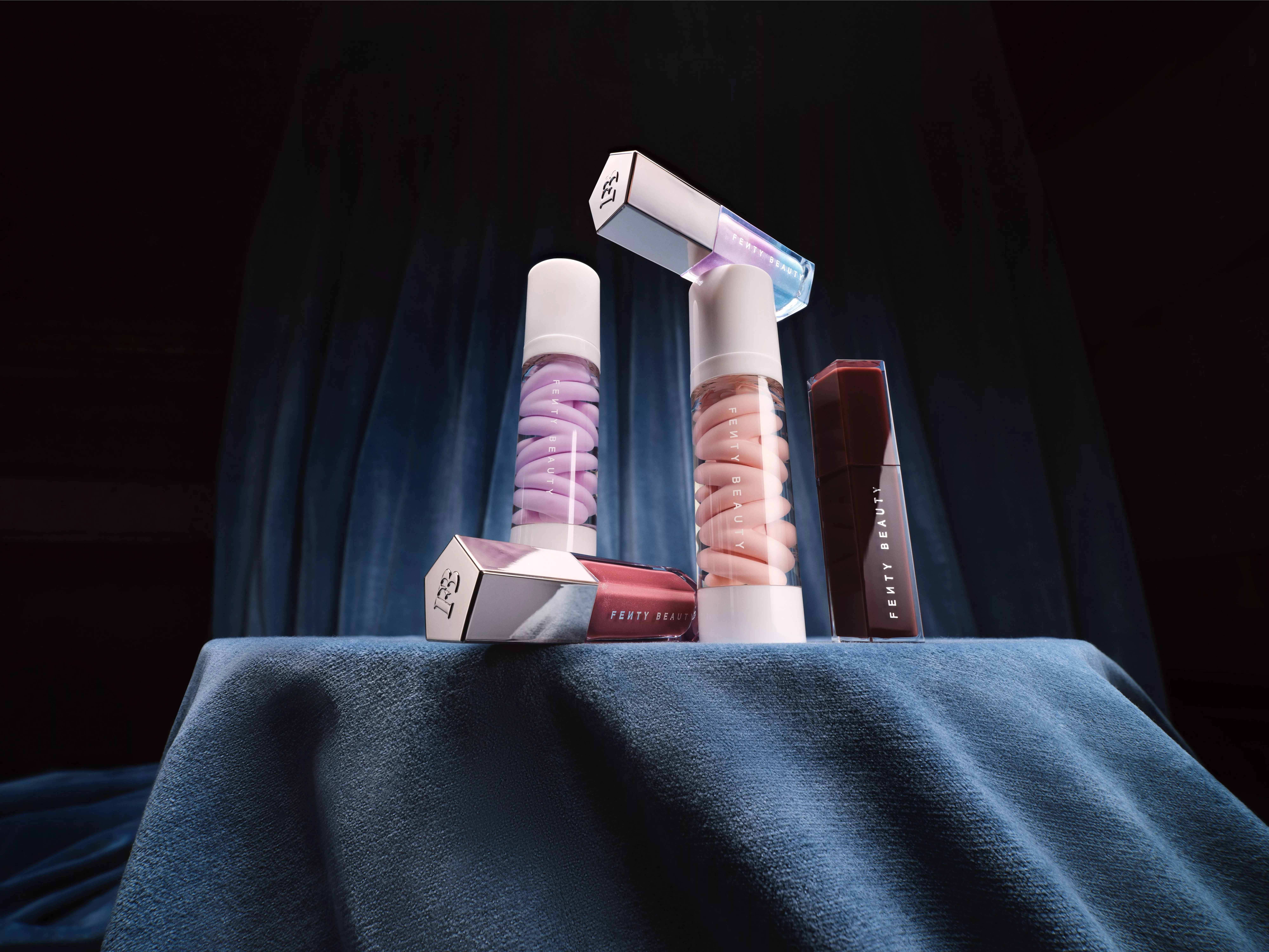 Fenty beauty products stacked on a blue fabric background