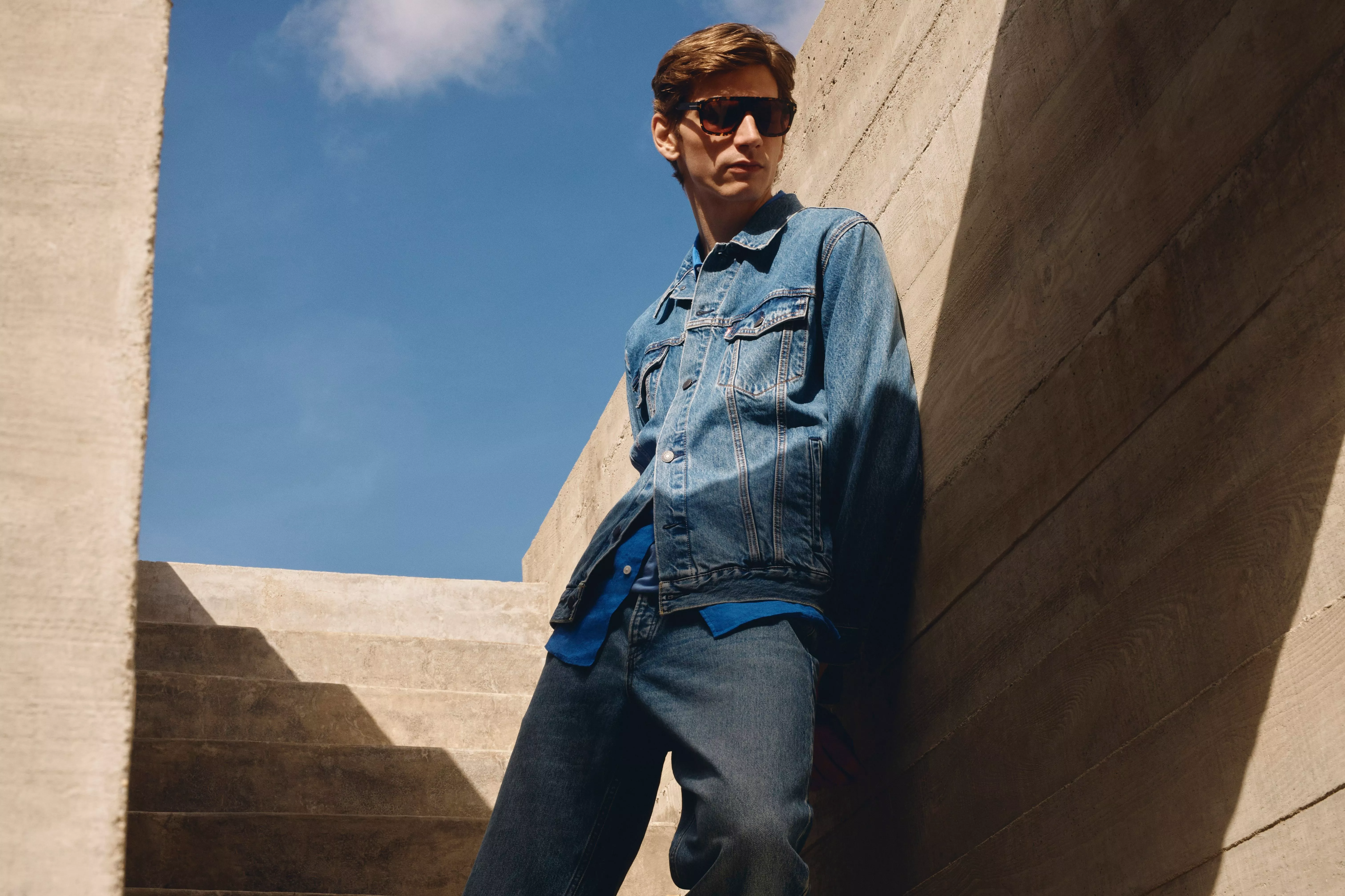 Model wearing full denim outfit leant against a concrete wall
