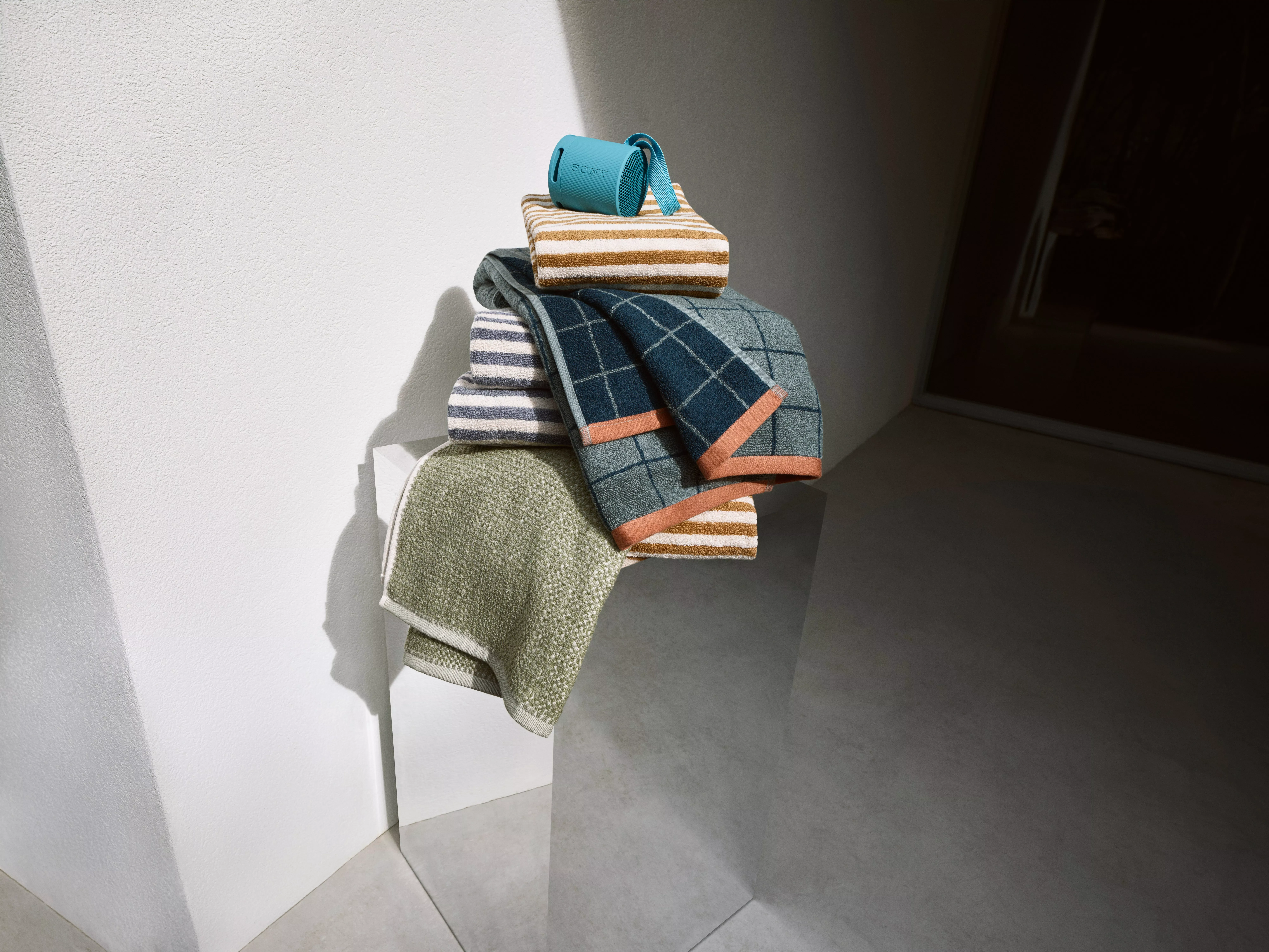 Pile of towels on a mirrored plinth with a portable speaker