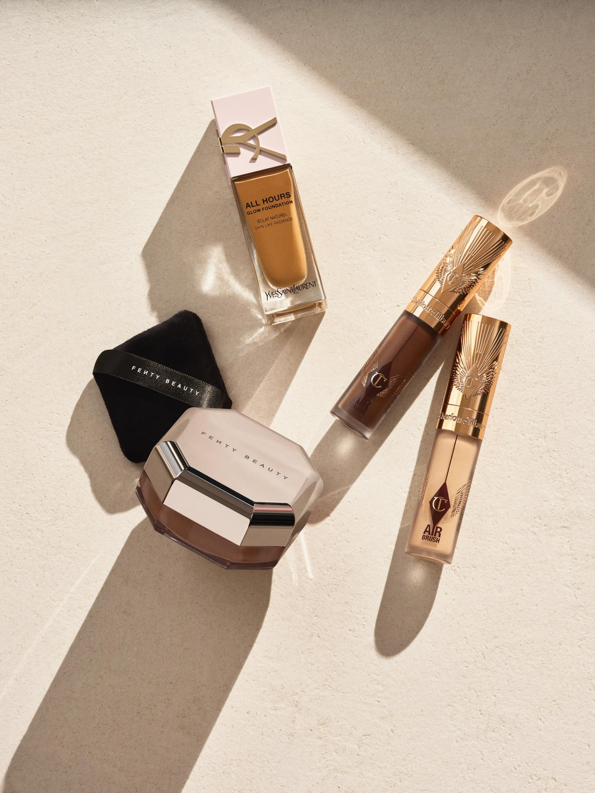 Luxury makeup essentials in sunlight: foundation bottle, compact powder and concealer tubes on a neutral surface