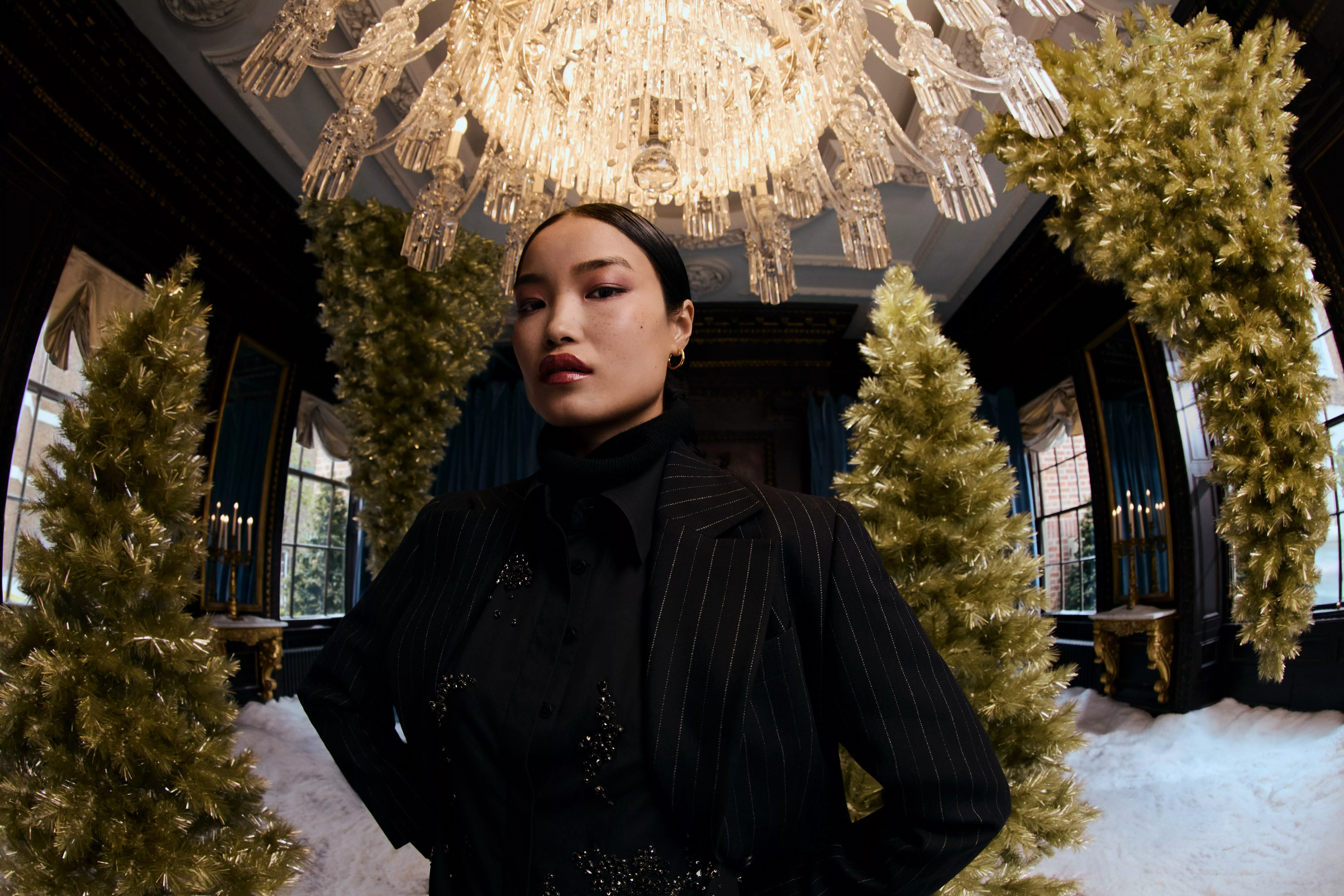 woman wearing stripe jacket with embellished blouse against a background of Christmas trees