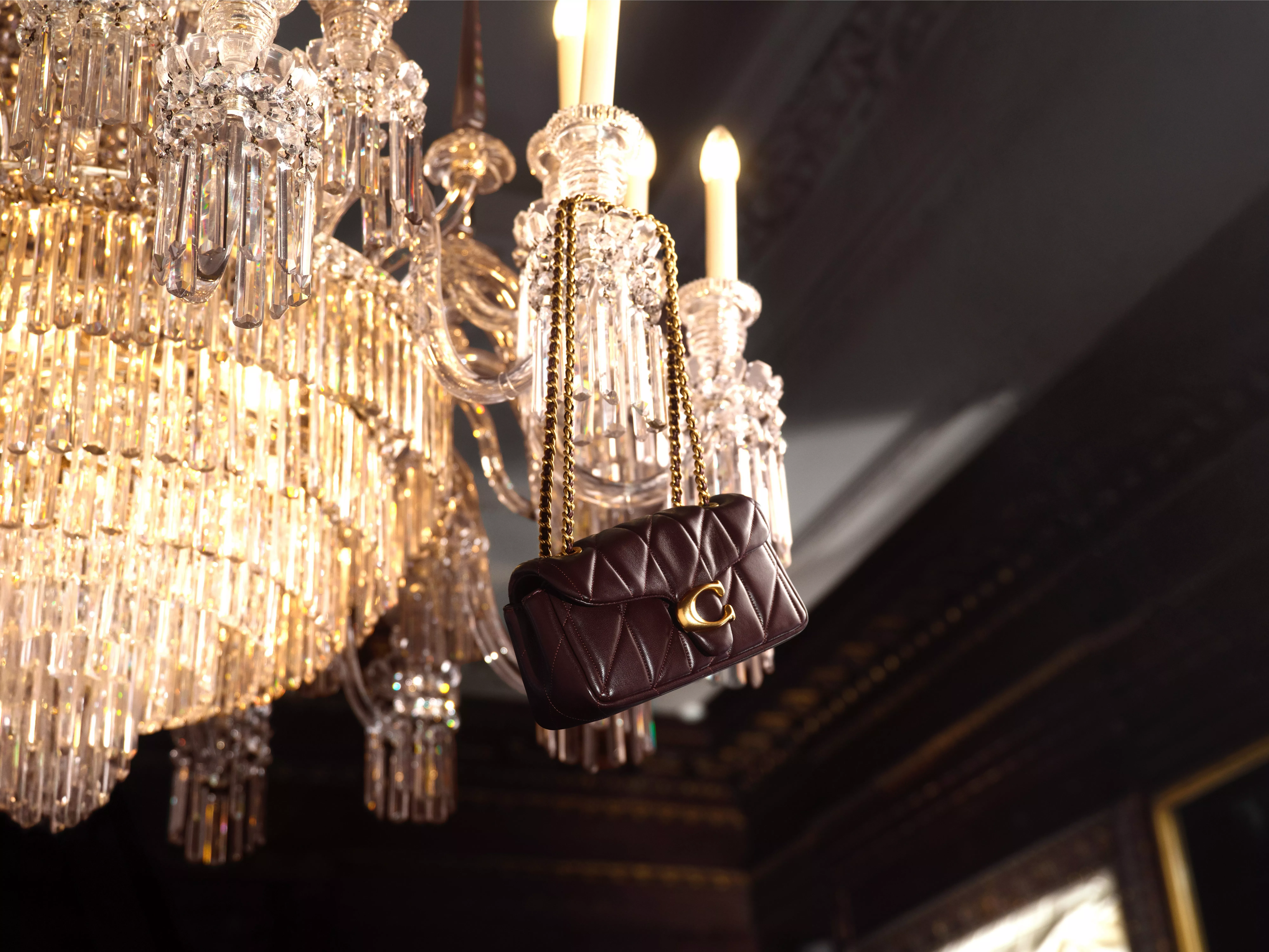 brown Coach handbag with gold chain strap hanging from a chandelier